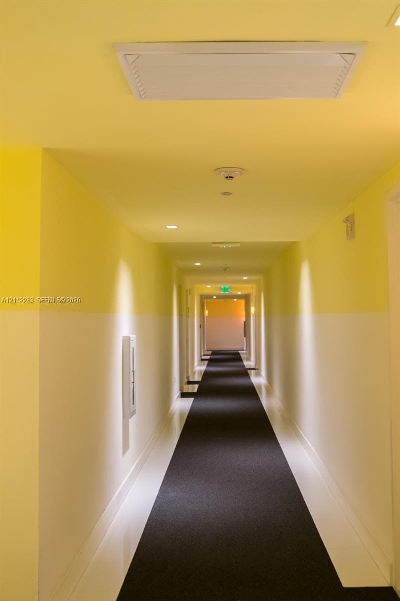 Hallway featuring two-tone wall paint, recessed ceiling lighting, a flush-mount overhead HVAC unit, integrated fire safety components, and dark wall-to-wall carpeting