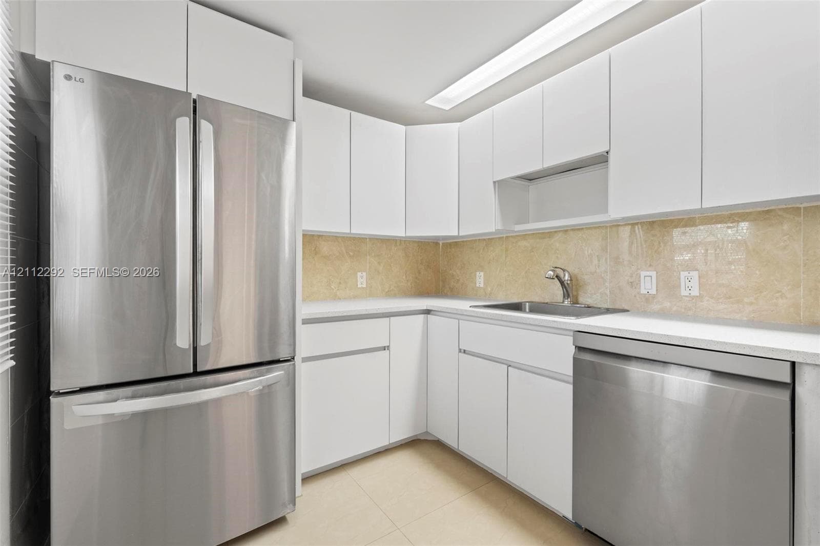 Kitchen featuring flat-panel white cabinetry, stainless steel appliances, neutral stone-finish backsplash, and an undermount sink with a gooseneck faucet