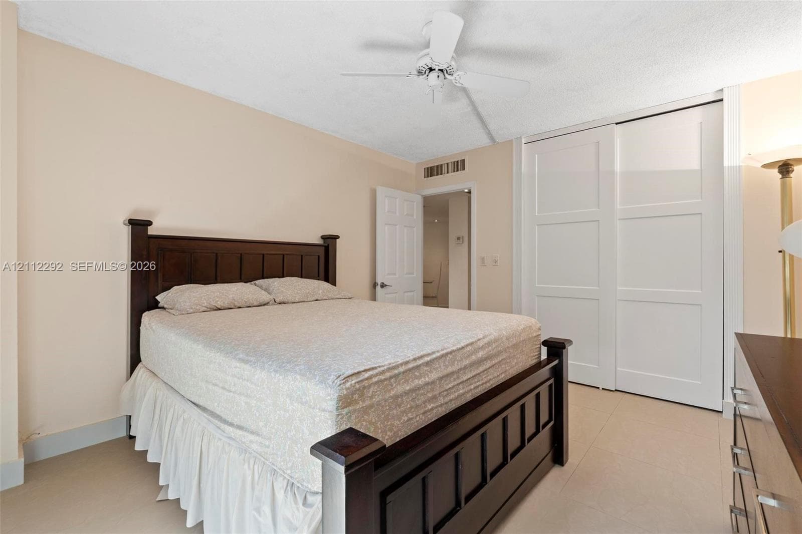 Neutral-toned room featuring tile flooring, a white ceiling fan, and sliding panel closet doors