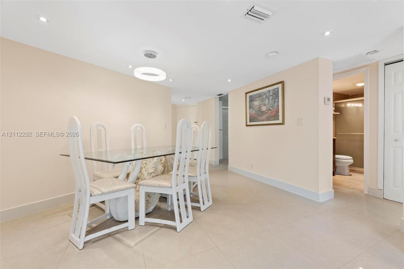 Open-concept area featuring light-toned tile flooring, recessed ceiling lighting, a modern circular LED pendant fixture, and a white paneled door