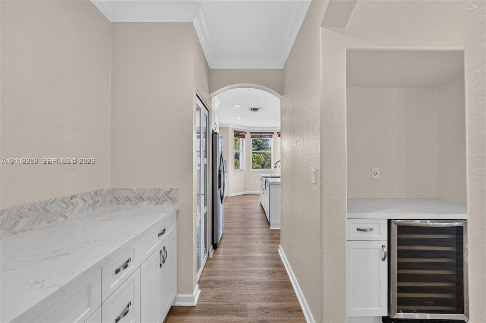 Butler pantry featuring white cabinetry, light-toned stone-finish countertops, a herringbone-patterned tile backsplash, and a built-in stainless steel beverage refrigerator