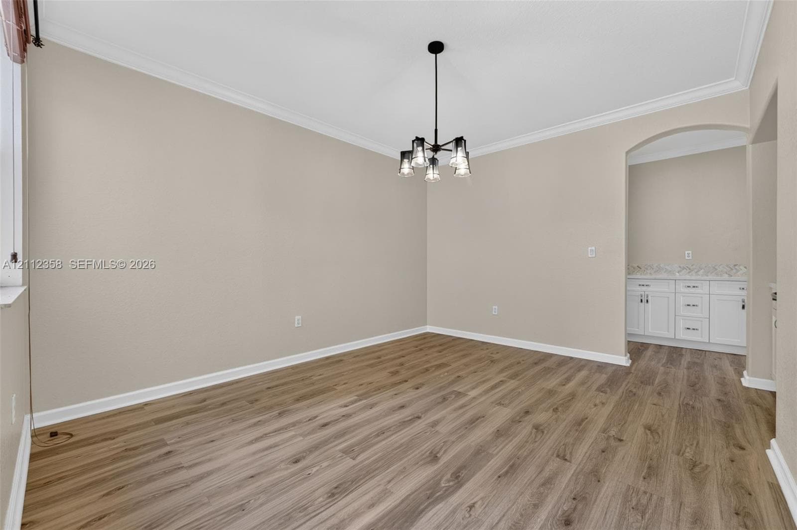 Interior space featuring wood-finish flooring, crown molding, a multi-light pendant fixture, and a built-in cabinetry unit with a countertop