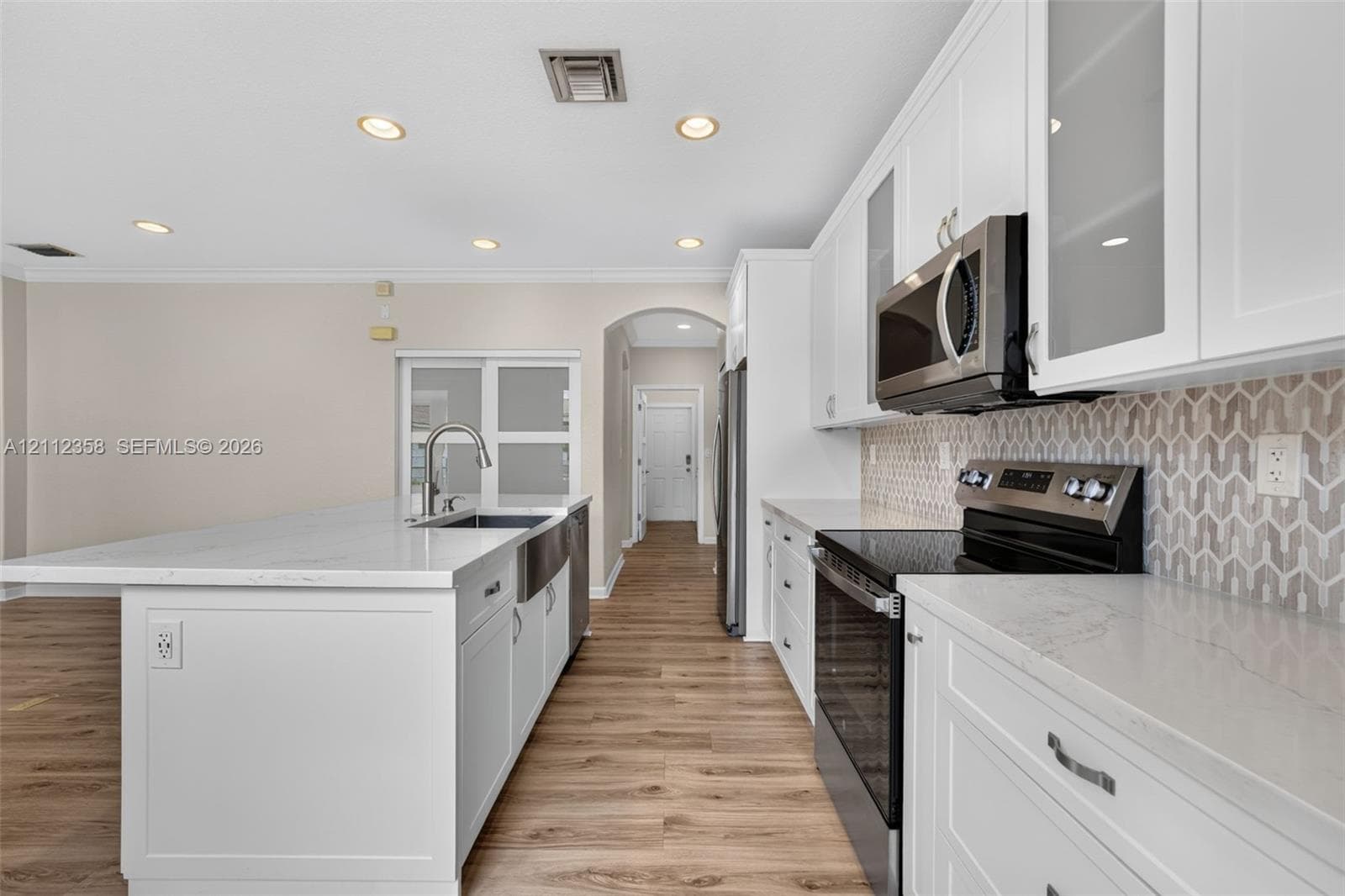 Kitchen featuring white cabinetry, stone-look countertops, stainless steel appliances, a farmhouse-style sink, and patterned tile backsplash