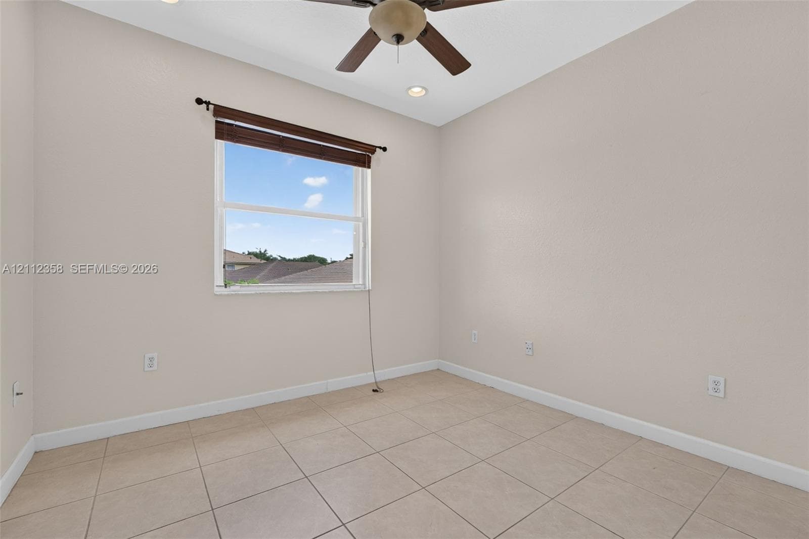 Neutral-toned interior space featuring tile flooring, a ceiling fan with integrated lighting, and a single-pane window with a roller shade