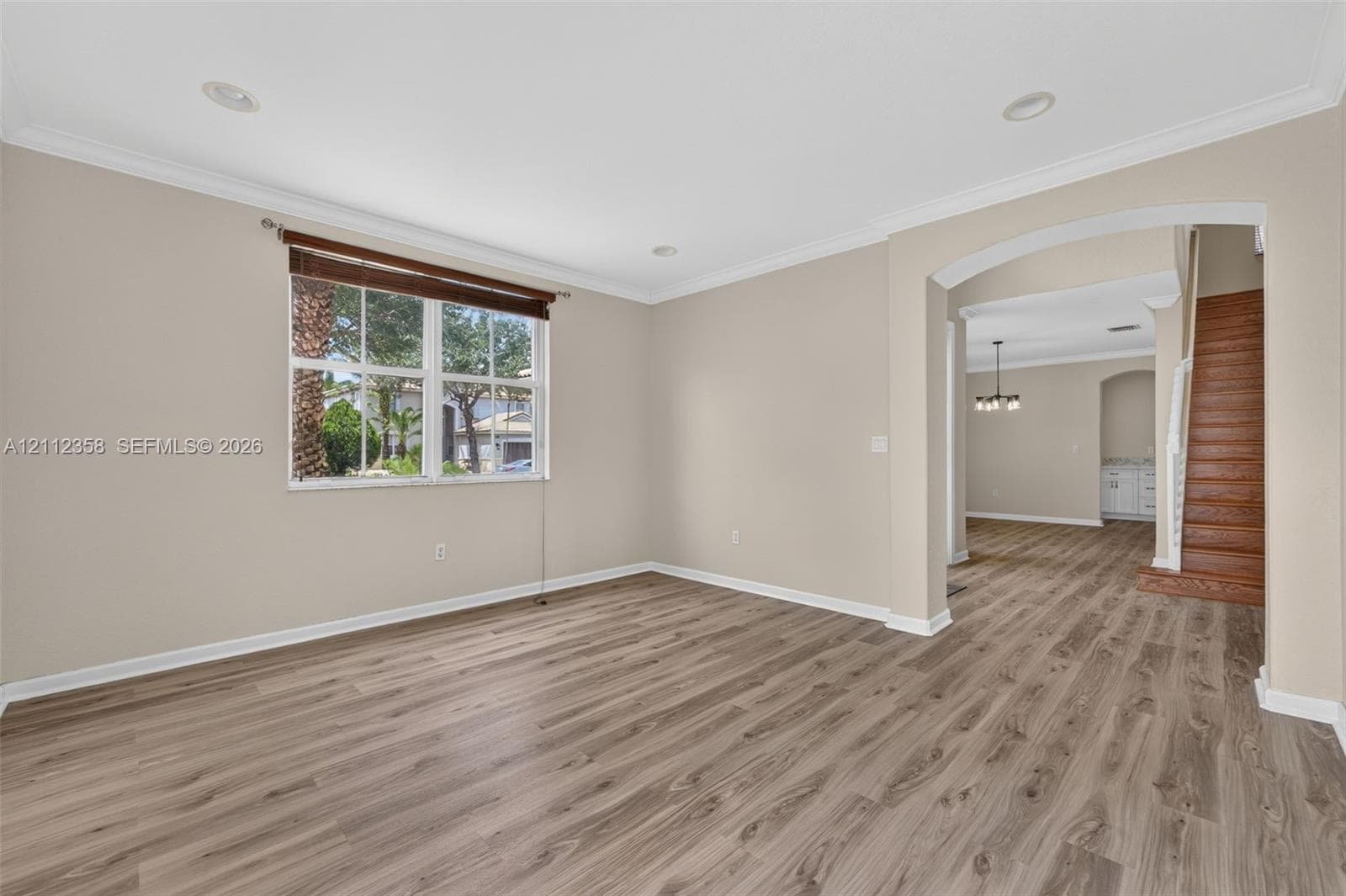 Open-concept space featuring wood-finish flooring, crown molding, recessed lighting, and a prominent arched entryway with wood-finish staircase