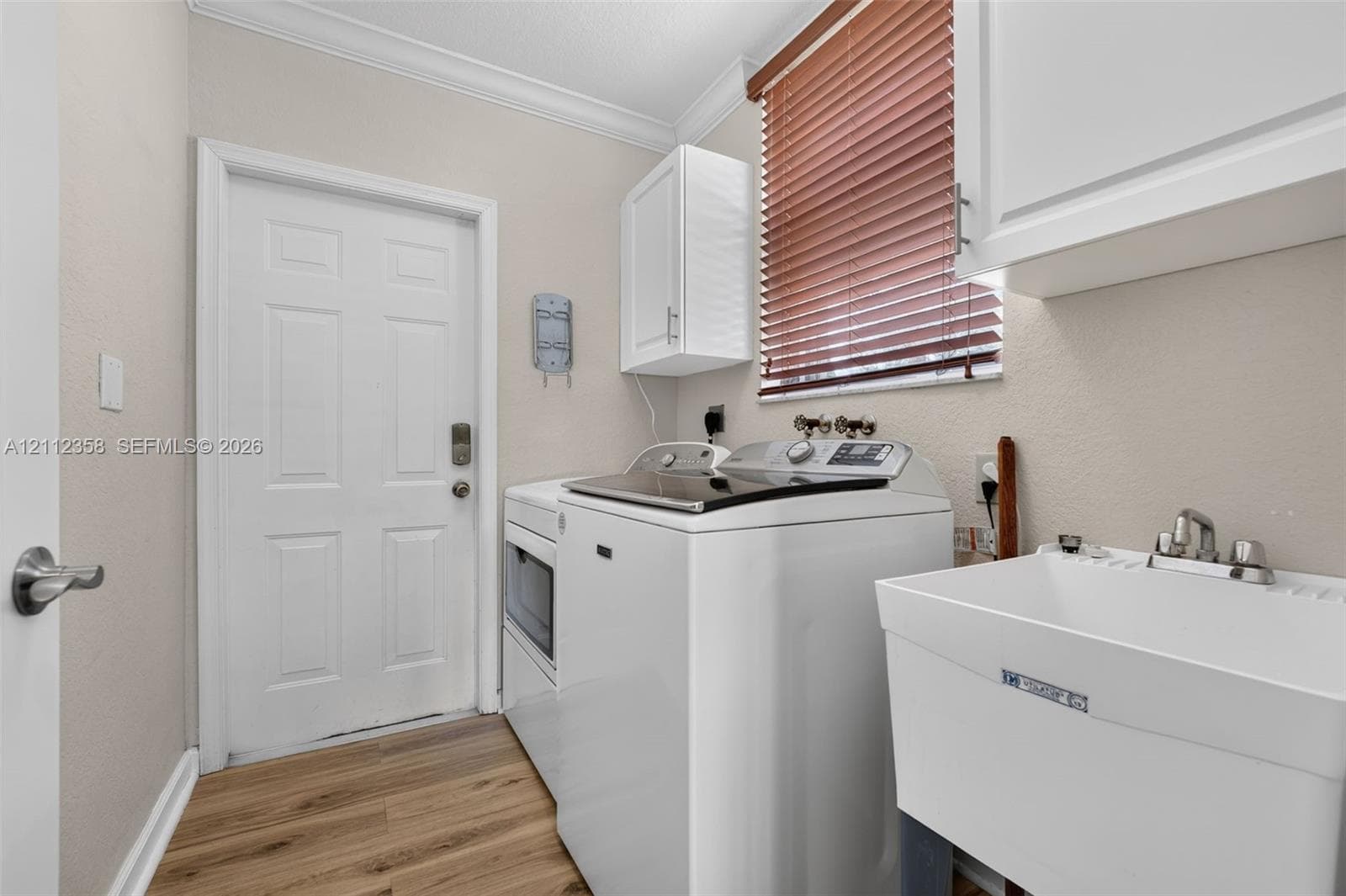 Laundry room featuring wood-finish flooring, white cabinetry, a utility sink, and window blinds
