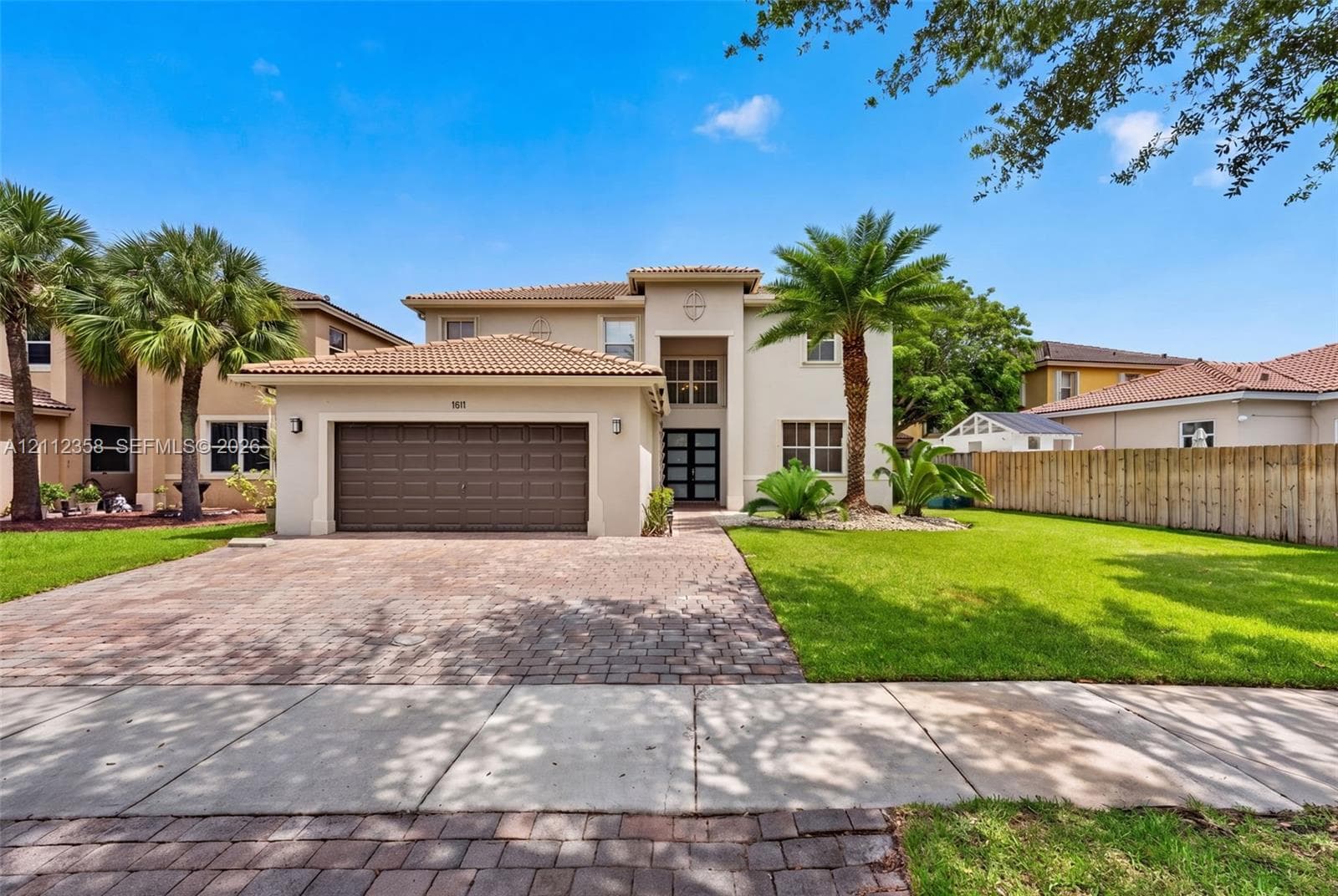 Stucco exterior featuring a dual-pitch tile roof, paver driveway, attached two-car garage, and manicured landscaping