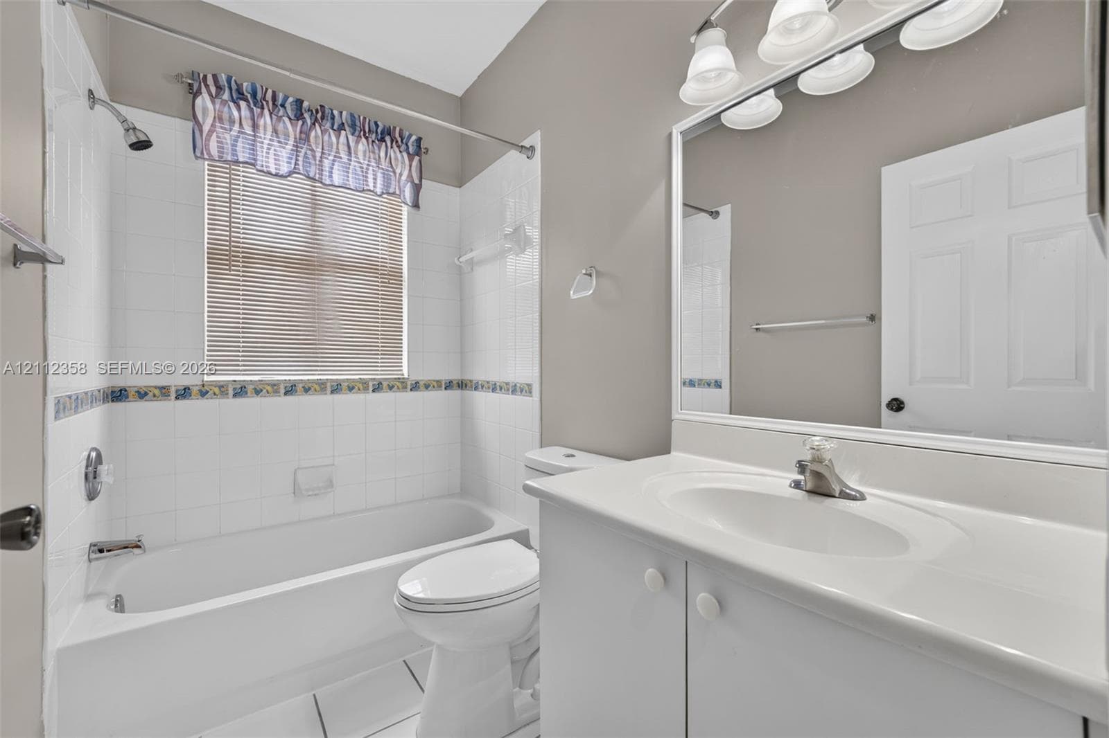 Bathroom featuring a white vanity with an integrated basin, a large wall-mounted mirror, a tub-shower combination with ceramic tile surround, and tile flooring