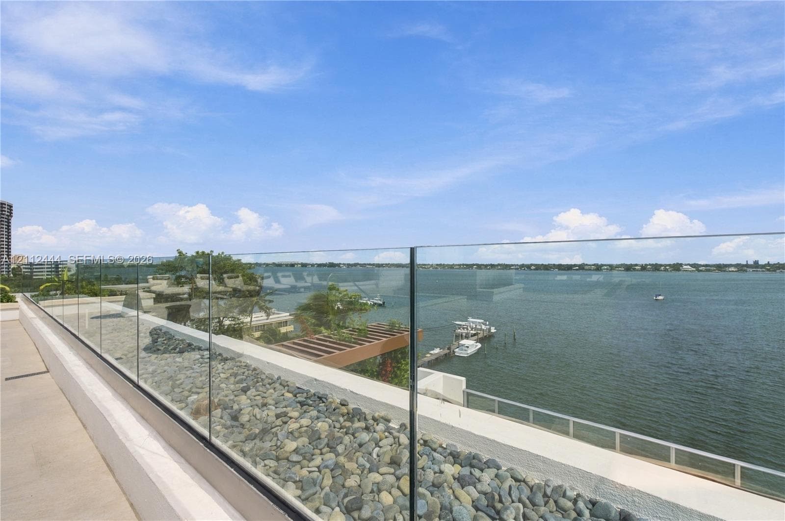 Elevated balcony featuring a frameless glass railing, stone-finished flooring, and water frontage
