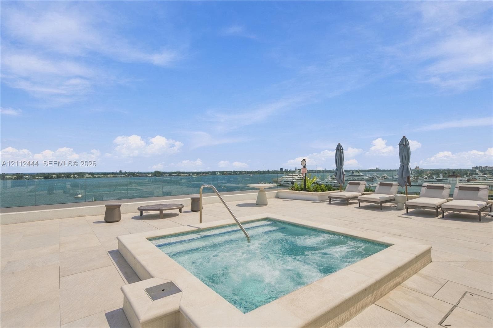 Rooftop terrace featuring stone tile flooring, an integrated jetted spa with a stainless steel handrail, and a frameless glass perimeter railing