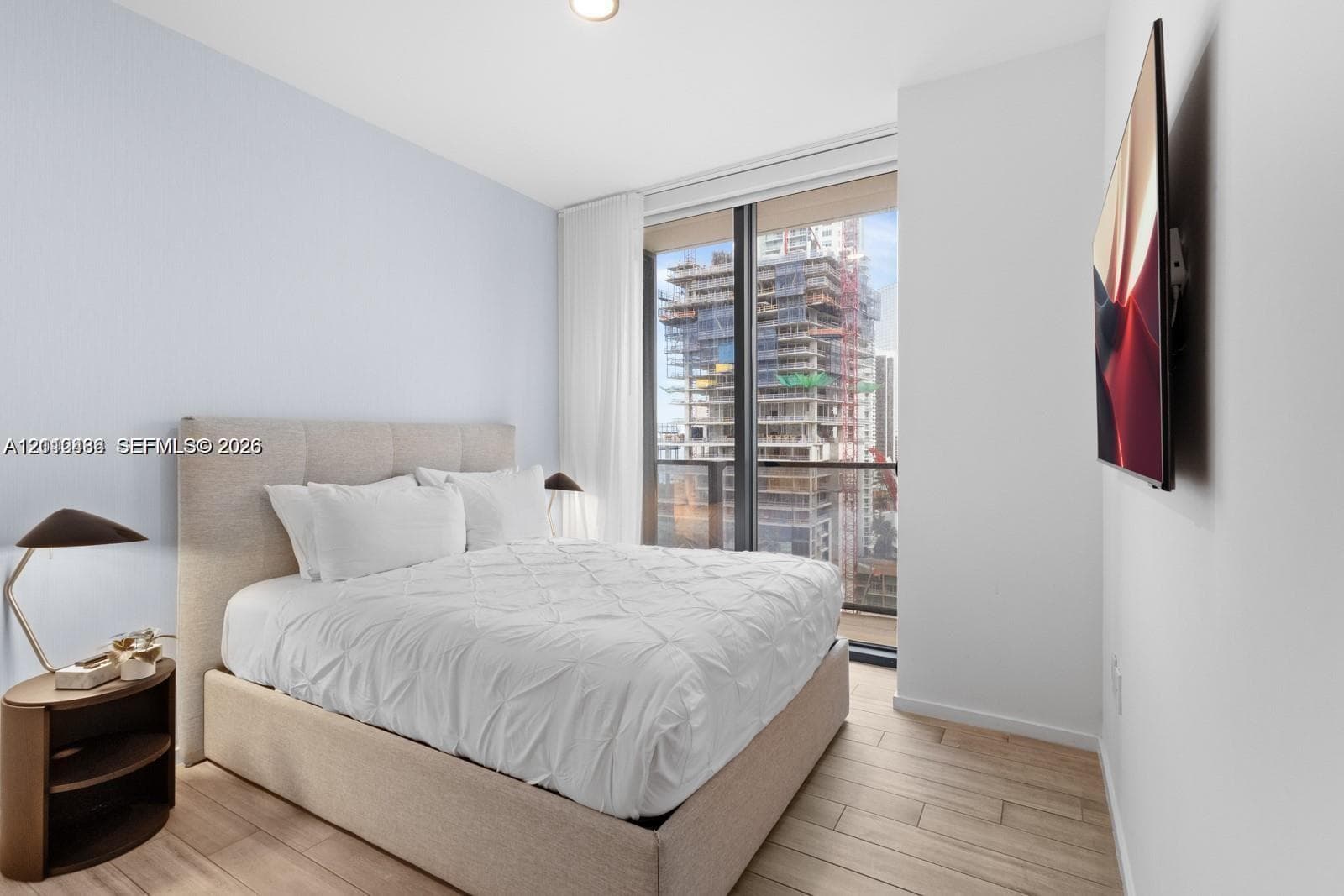 Floor-to-ceiling windows with access to a balcony, wood-finish flooring, and wall-mounted television hardware