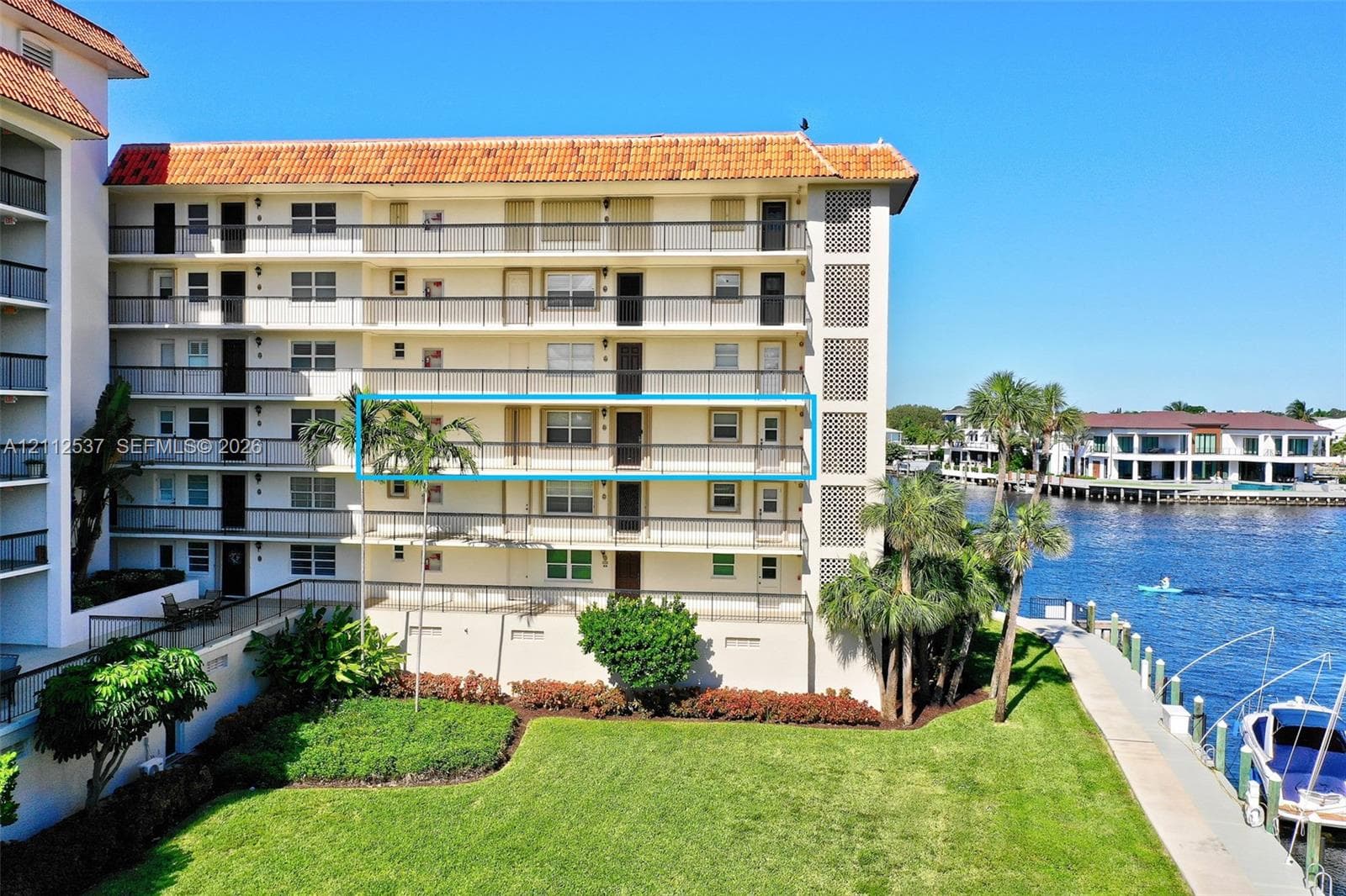 Multi-story waterfront residential building featuring a terracotta tile roof, wrap-around balconies with metal railings, and direct access to a private dock