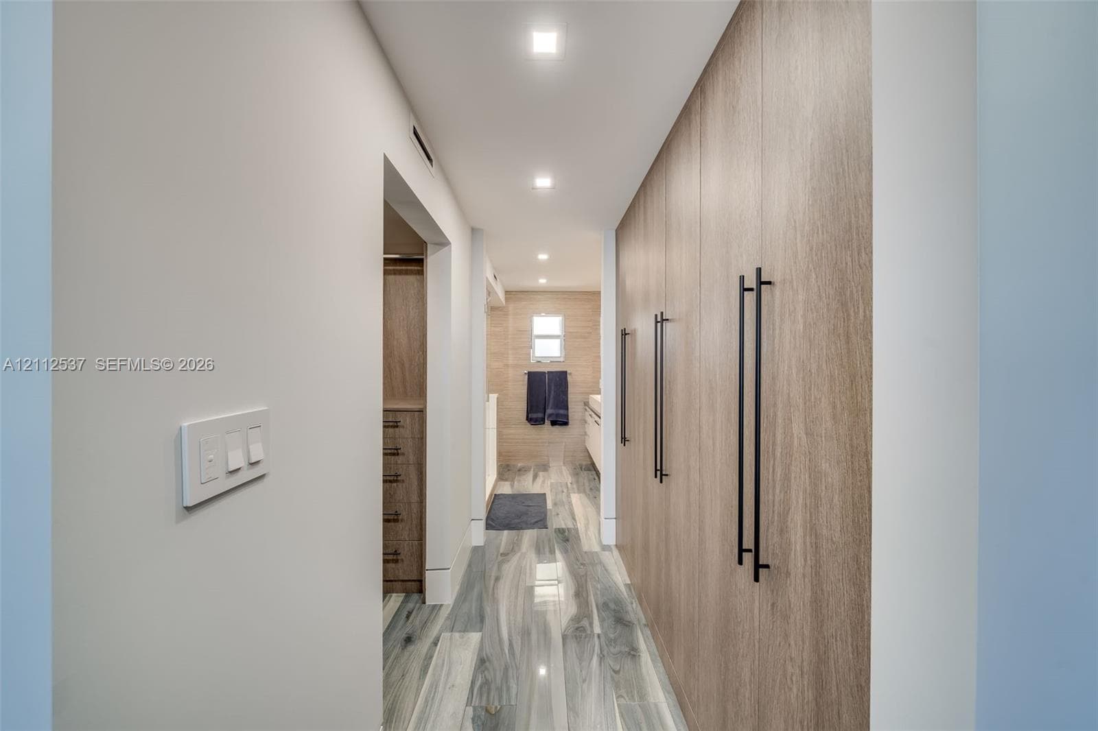 Floor-to-ceiling built-in wood-finish cabinetry featuring matte black hardware, recessed ceiling lighting, and porcelain tile flooring with a marble-pattern finish