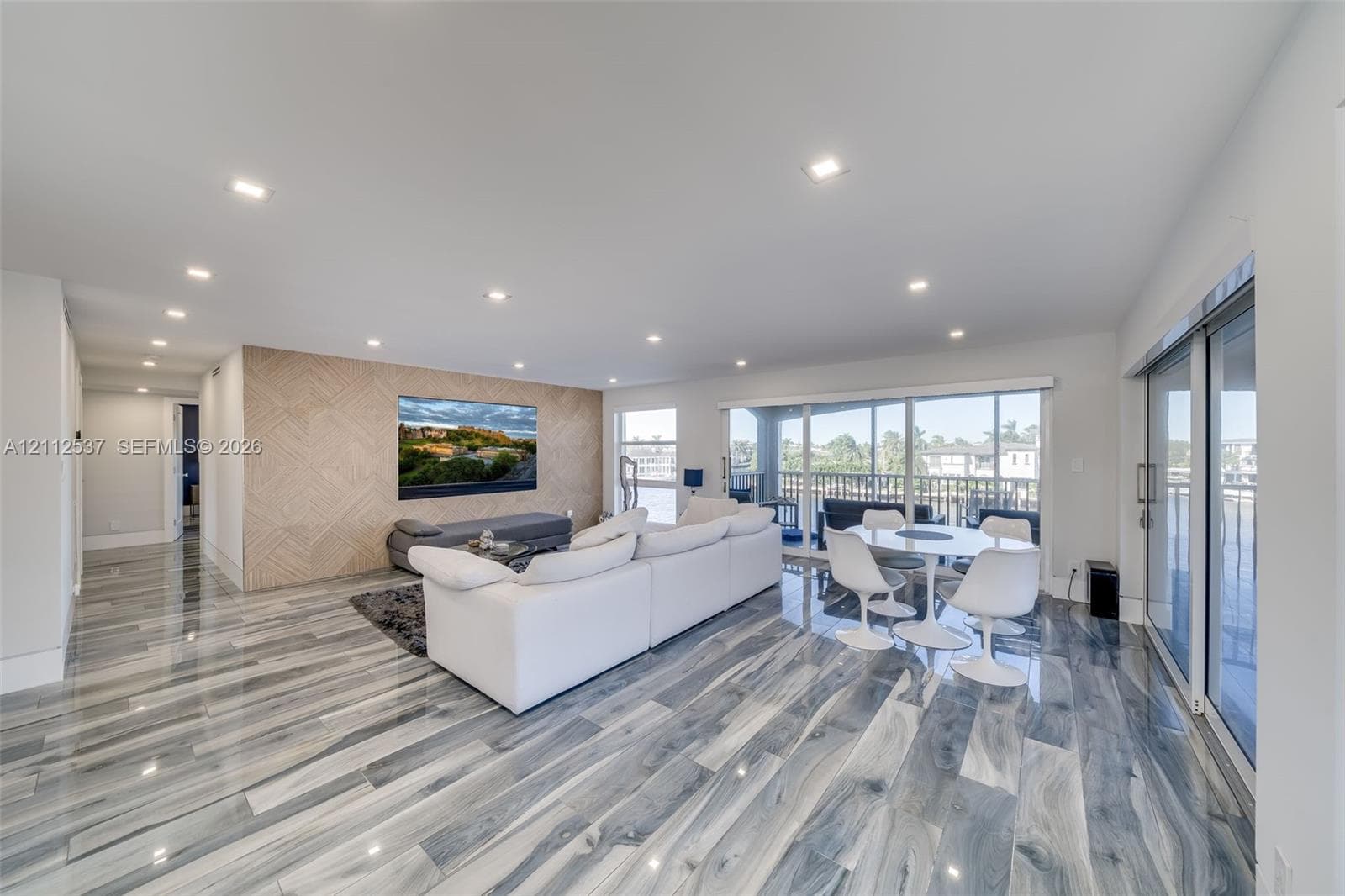 Open-concept room featuring polished stone-finish flooring, recessed lighting, a geometric wood-paneled accent wall, and floor-to-ceiling glass sliding doors