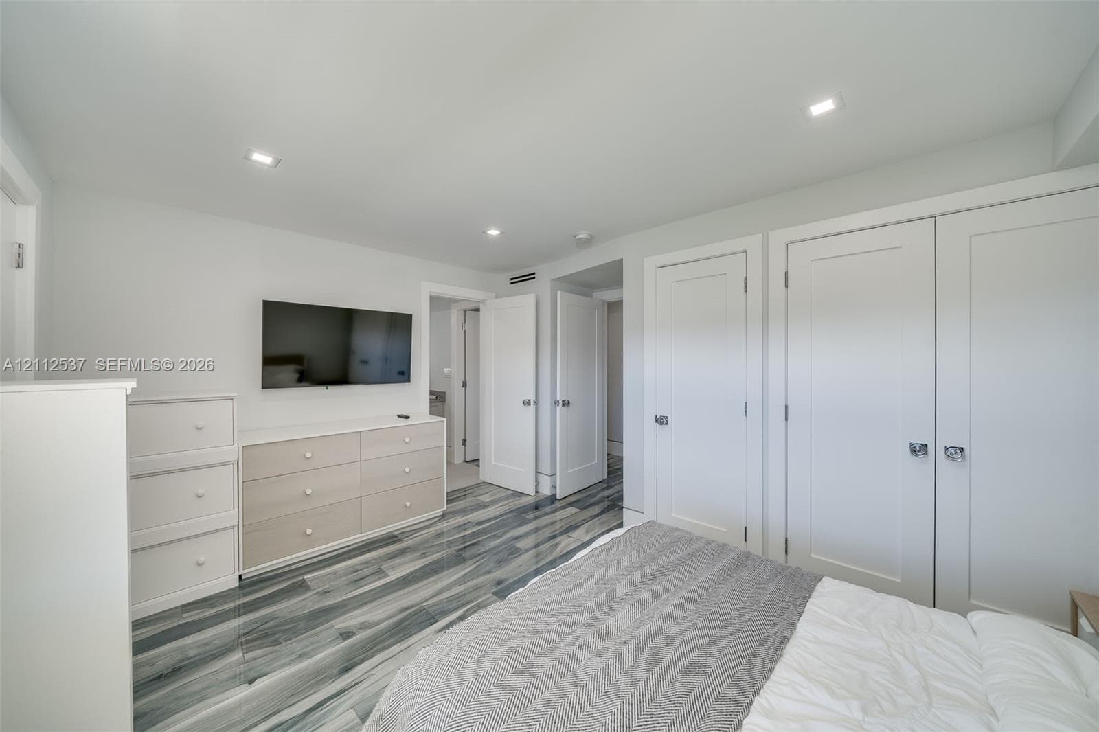 Wood-finish flooring with a multi-tonal pattern, recessed ceiling lighting, and double-door reach-in closet featuring shaker-style panels