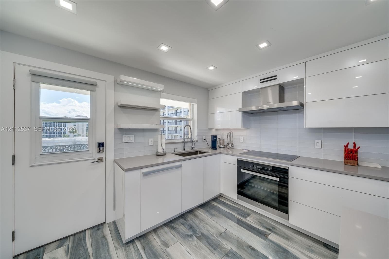 Kitchen featuring high-gloss white cabinetry, quartz countertops, stainless steel appliances, recessed lighting, and wood-finish tile flooring