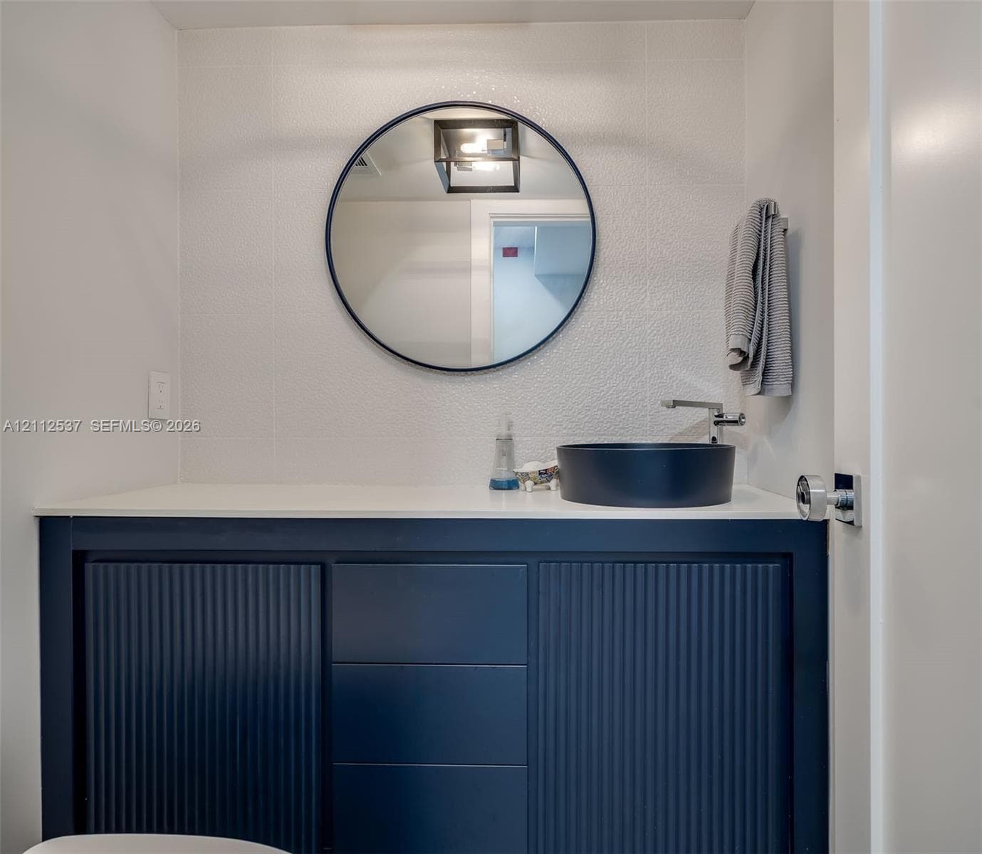 Navy blue fluted vanity with a white countertop, round black-framed mirror, and matte black vessel sink