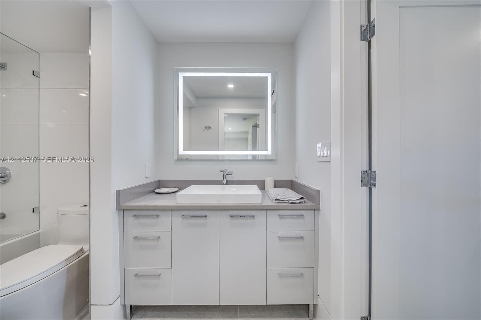 Bathroom vanity featuring flat-panel cabinetry, a rectangular vessel sink, solid-surface countertop, and an integrated LED-backlit mirror