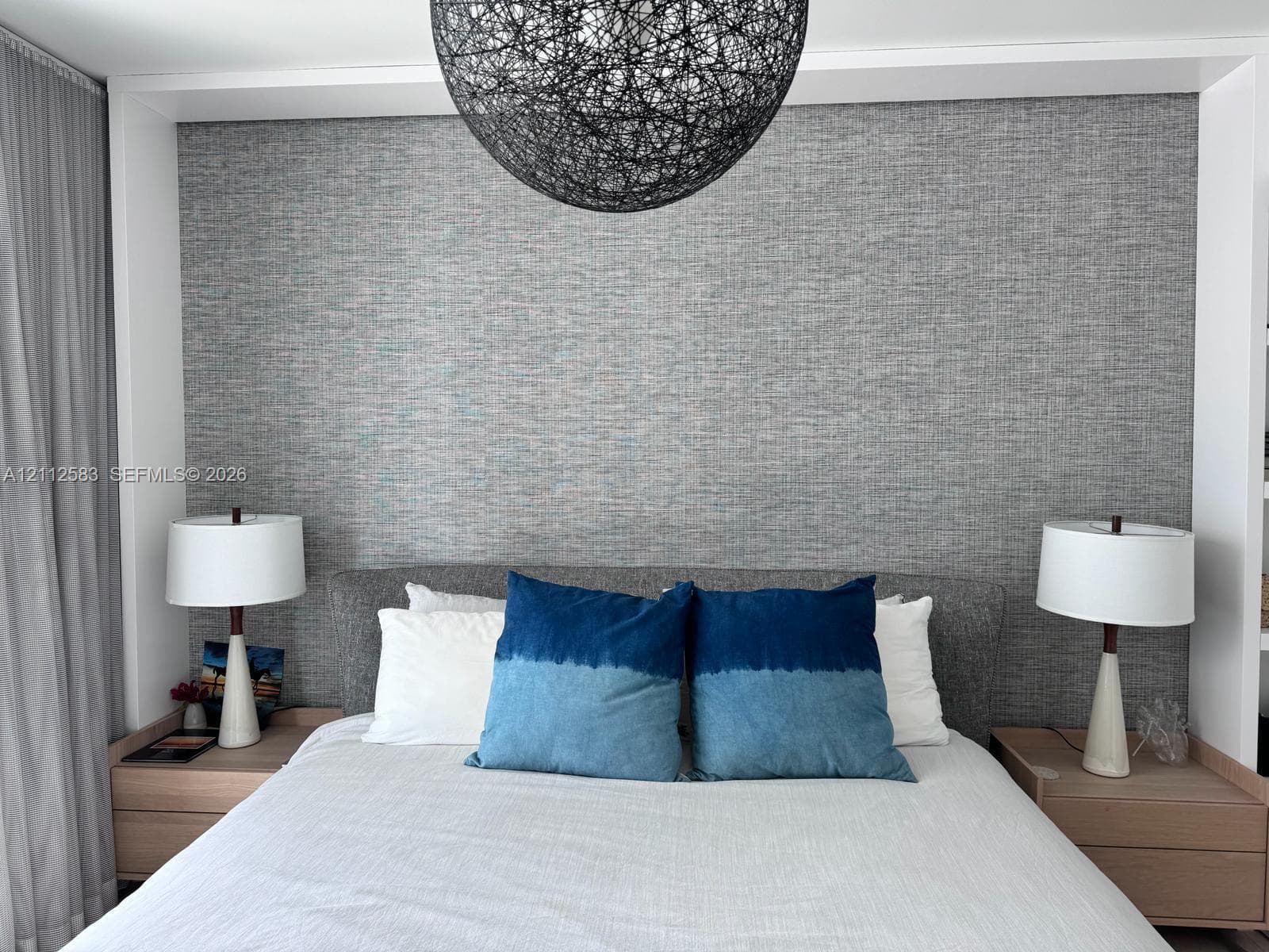 Textured gray wall accent, recessed built-in wood-finish nightstands, and spherical overhead pendant light fixture
