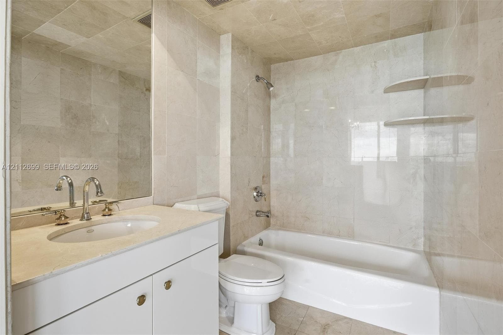 Full-height stone tile wall treatments, integrated floating stone shelving, undermount sink with polished chrome hardware, custom white cabinetry with stone countertop, and recessed ceiling lighting