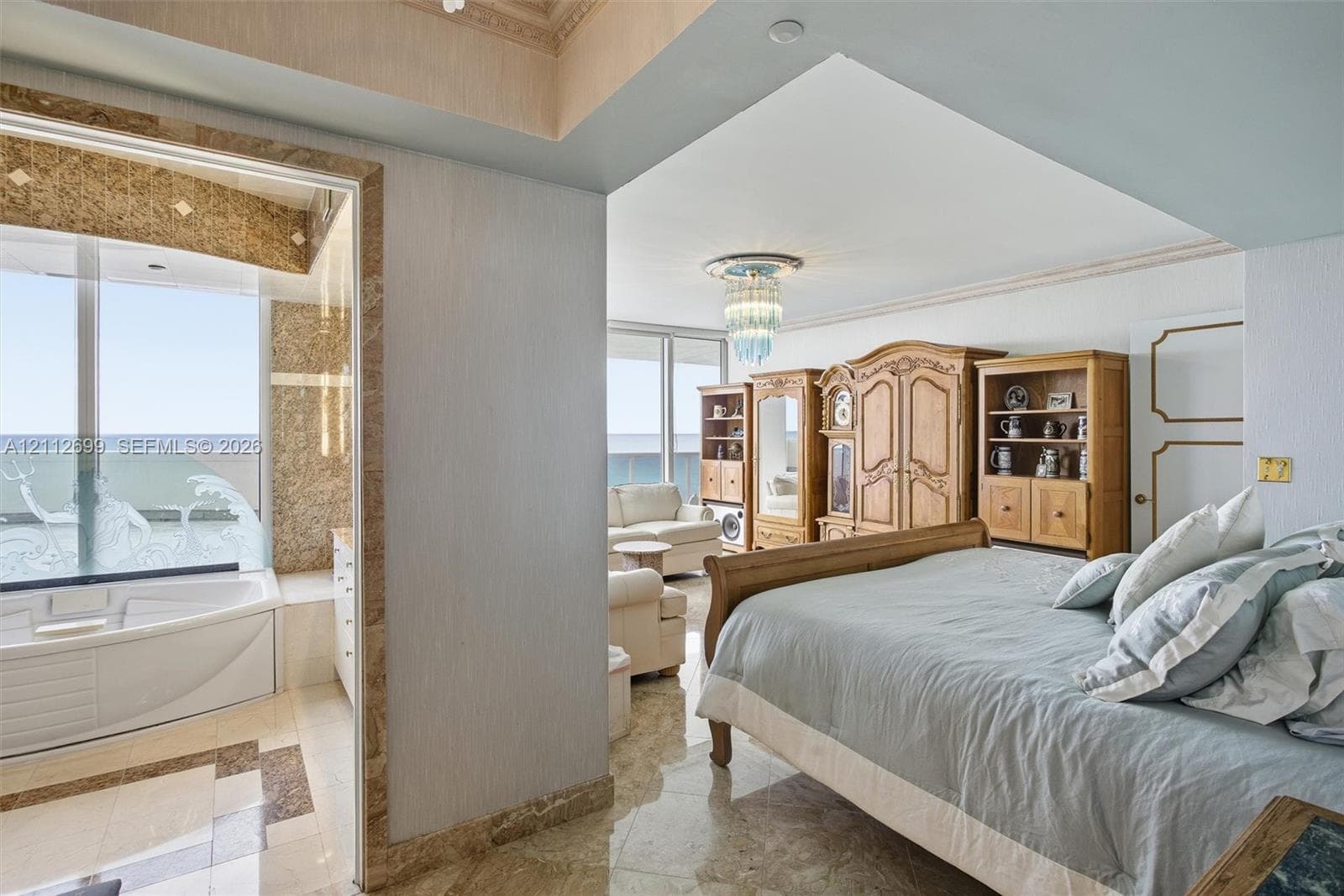 Polished stone flooring, crown molding, built-in recessed lighting, decorative crystal-style chandelier, and jetted corner soaking tub featuring stone tile surround