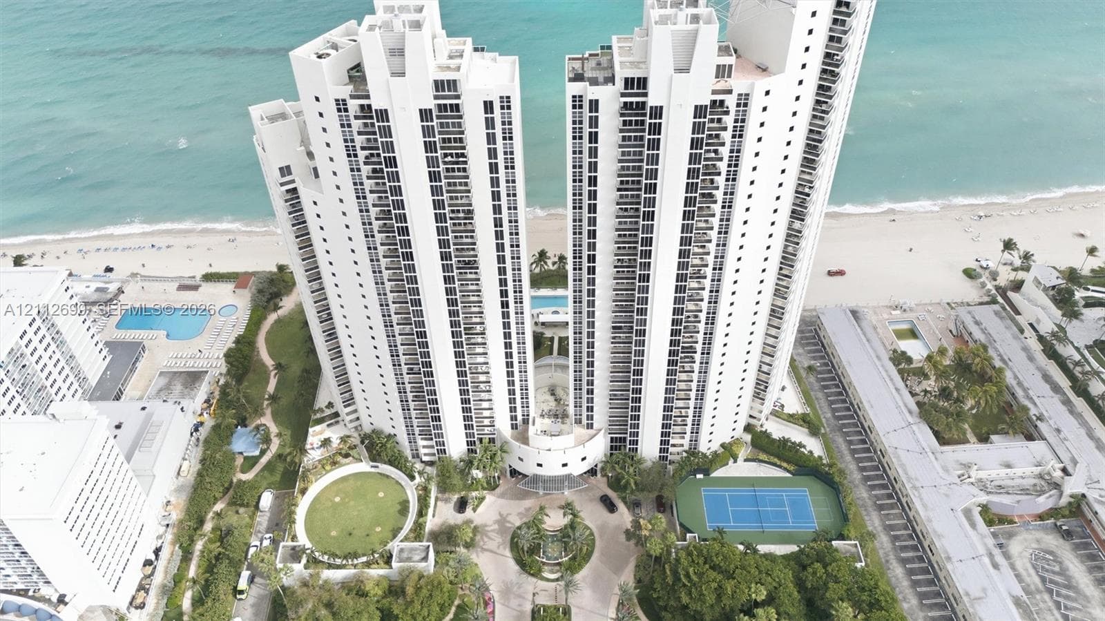 High-rise residential towers featuring direct oceanfront access, a private tennis court, an outdoor swimming pool, and landscaped grounds