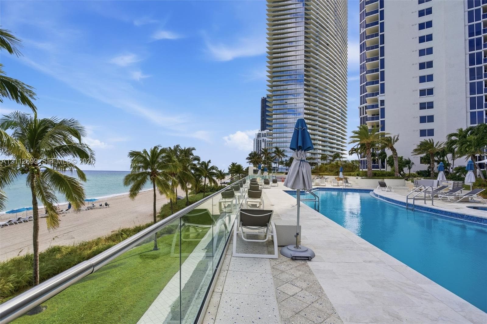 Oceanfront swimming pool with tiled surround, glass panel railing, and direct sandy beach access