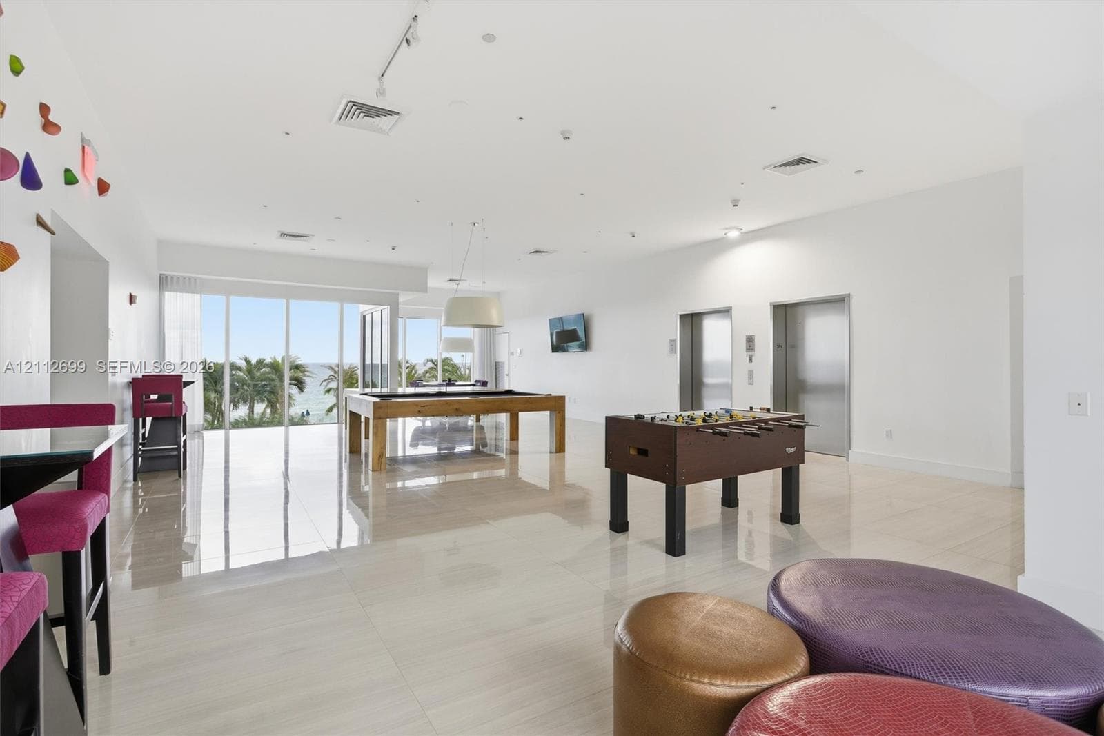 Open-concept common area featuring high-gloss tile flooring, floor-to-ceiling glass wall, recessed track lighting, and dual elevator access