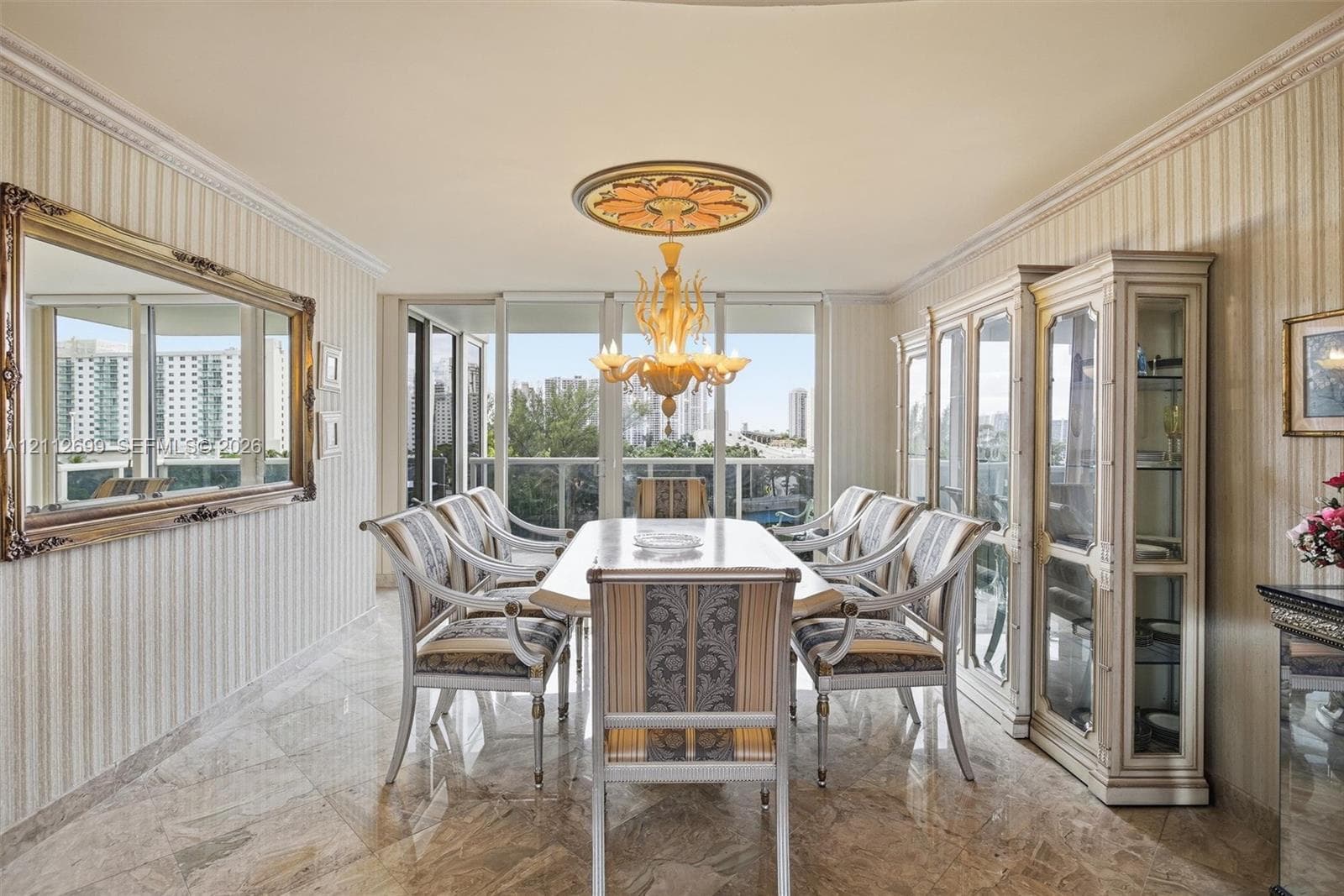 Dining area featuring polished stone flooring, custom built-in cabinetry, crown molding, a decorative ceiling medallion, and a chandelier