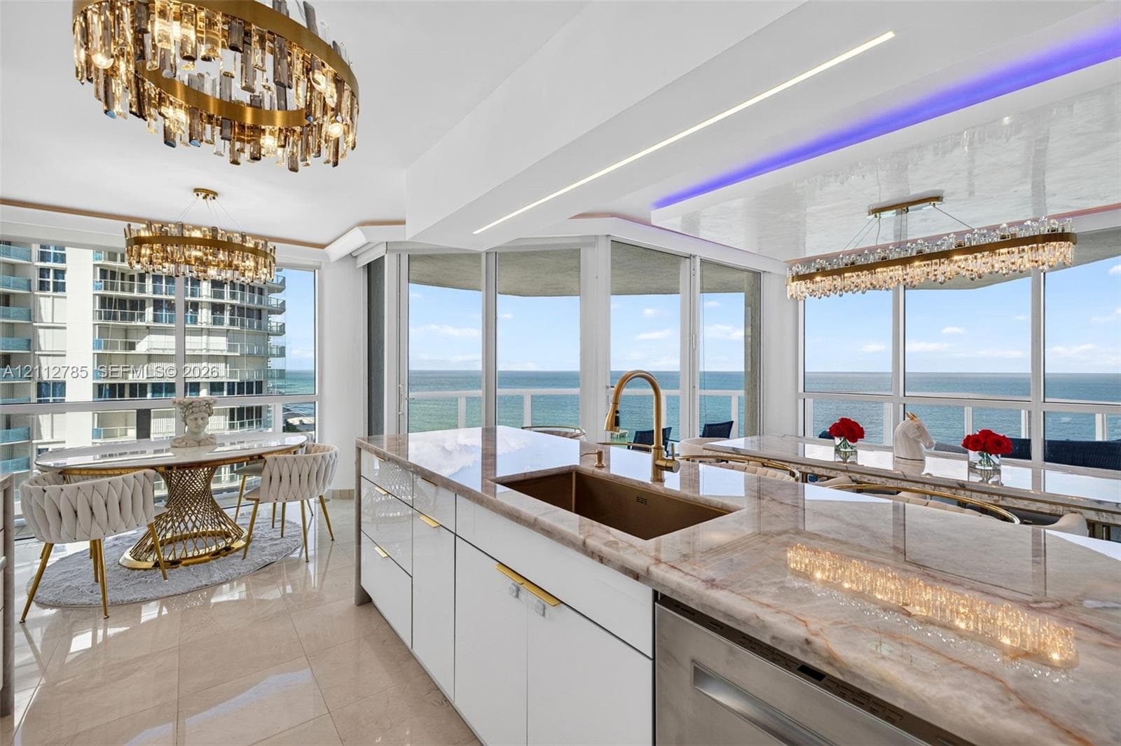 Kitchen featuring stone countertops, white flat-panel cabinetry, a metallic undermount sink with a gooseneck faucet, floor-to-ceiling glass walls, and tiered crystal chandeliers