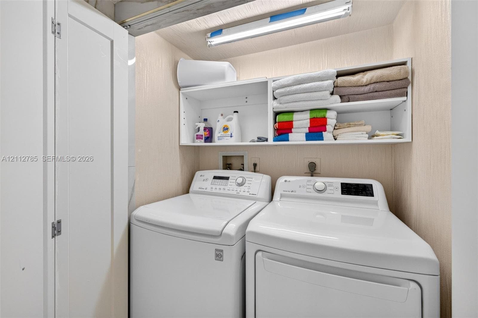 Laundry area featuring built-in white shelving, overhead task lighting, and bi-fold closet doors