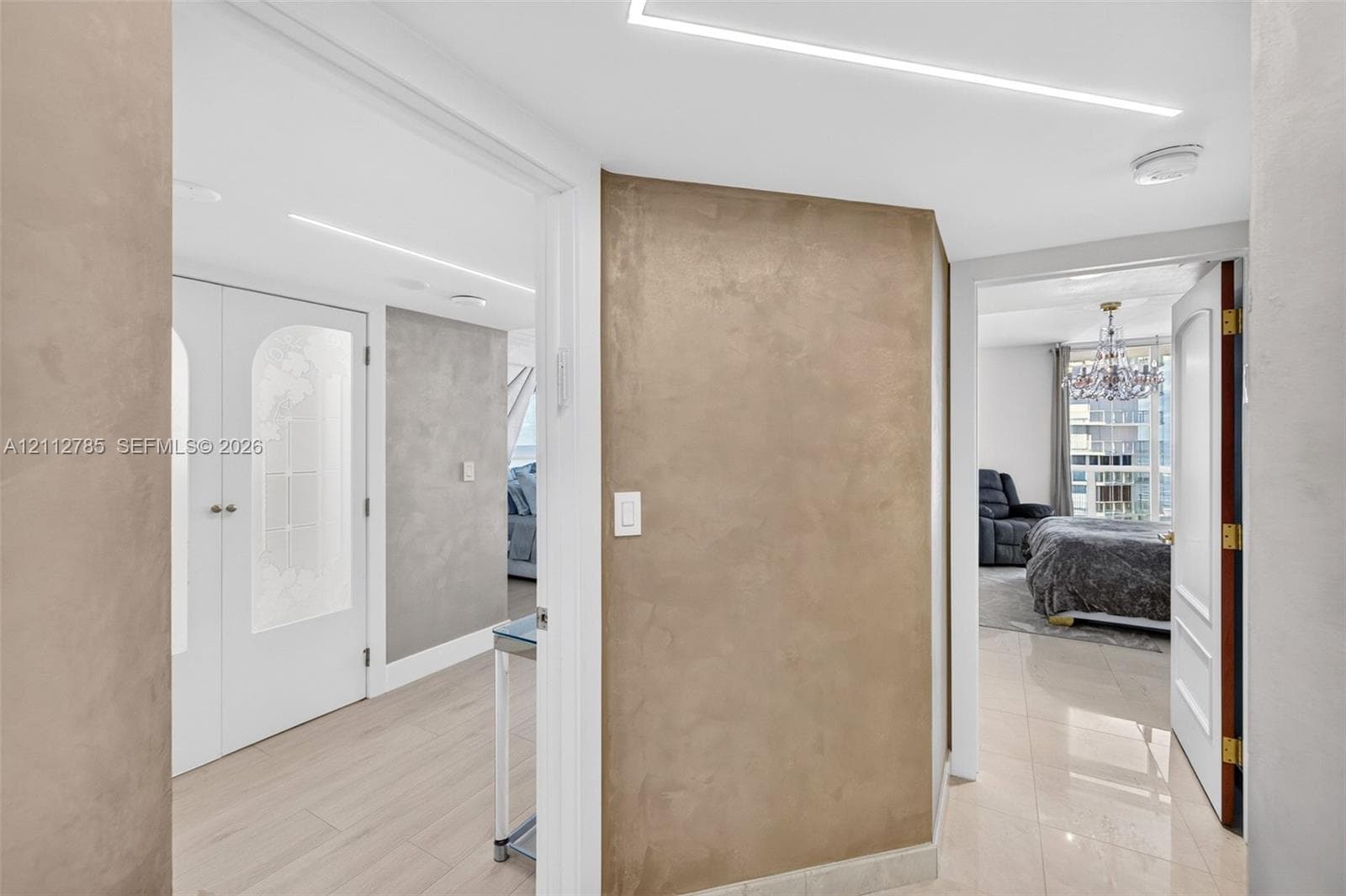 Textured plaster accent walls, recessed linear ceiling lighting, light-toned tile flooring, and interior doors featuring arched frosted glass panels