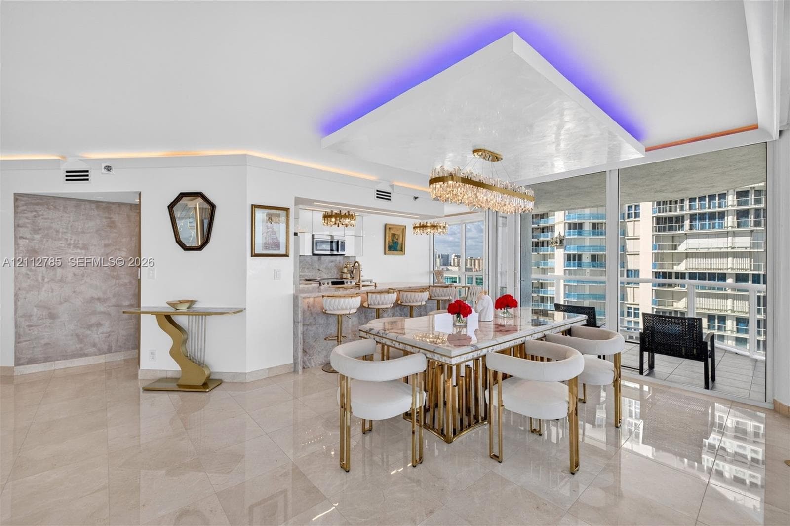 Open-concept area featuring polished tile flooring, a recessed ceiling detail with integrated accent lighting, a large crystal-style linear chandelier, and floor-to-ceiling glass windows