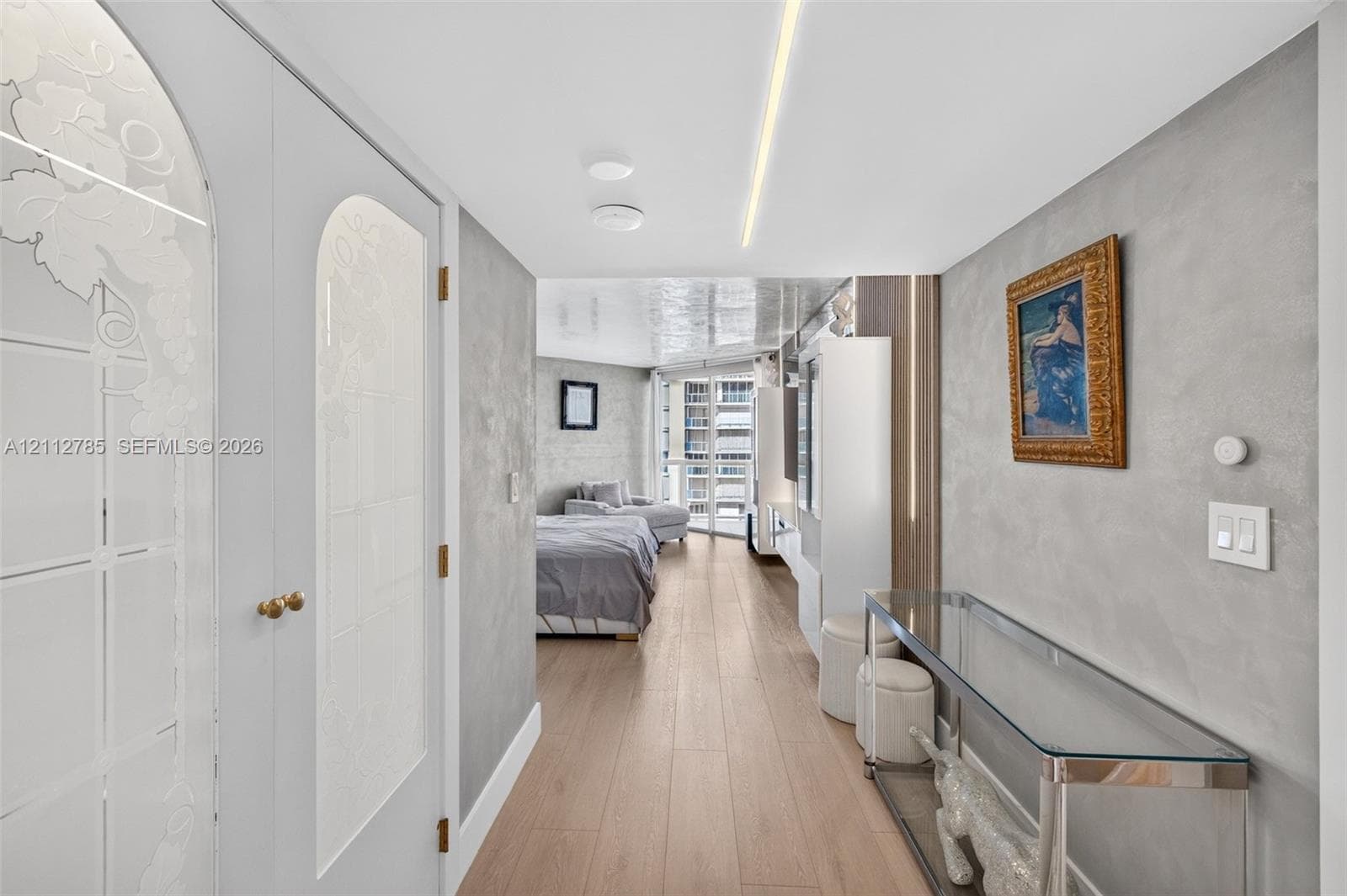Interior space featuring wood-finish flooring, textured metallic wall finishes, recessed linear ceiling lighting, and custom double doors with arched glass panels