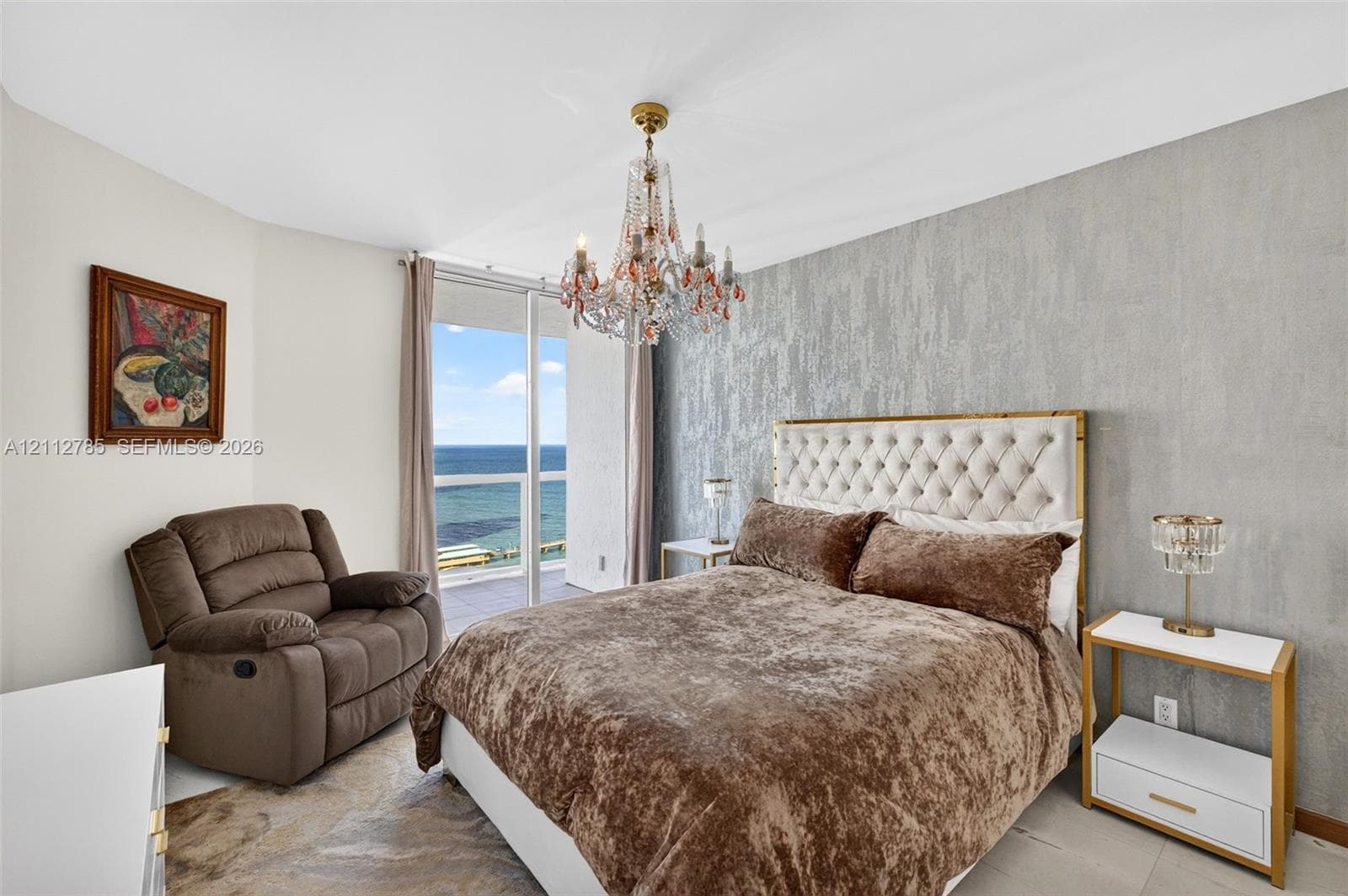 Floor-to-ceiling glass sliding doors with water scenery, intricate crystal chandelier, and textured accent wall