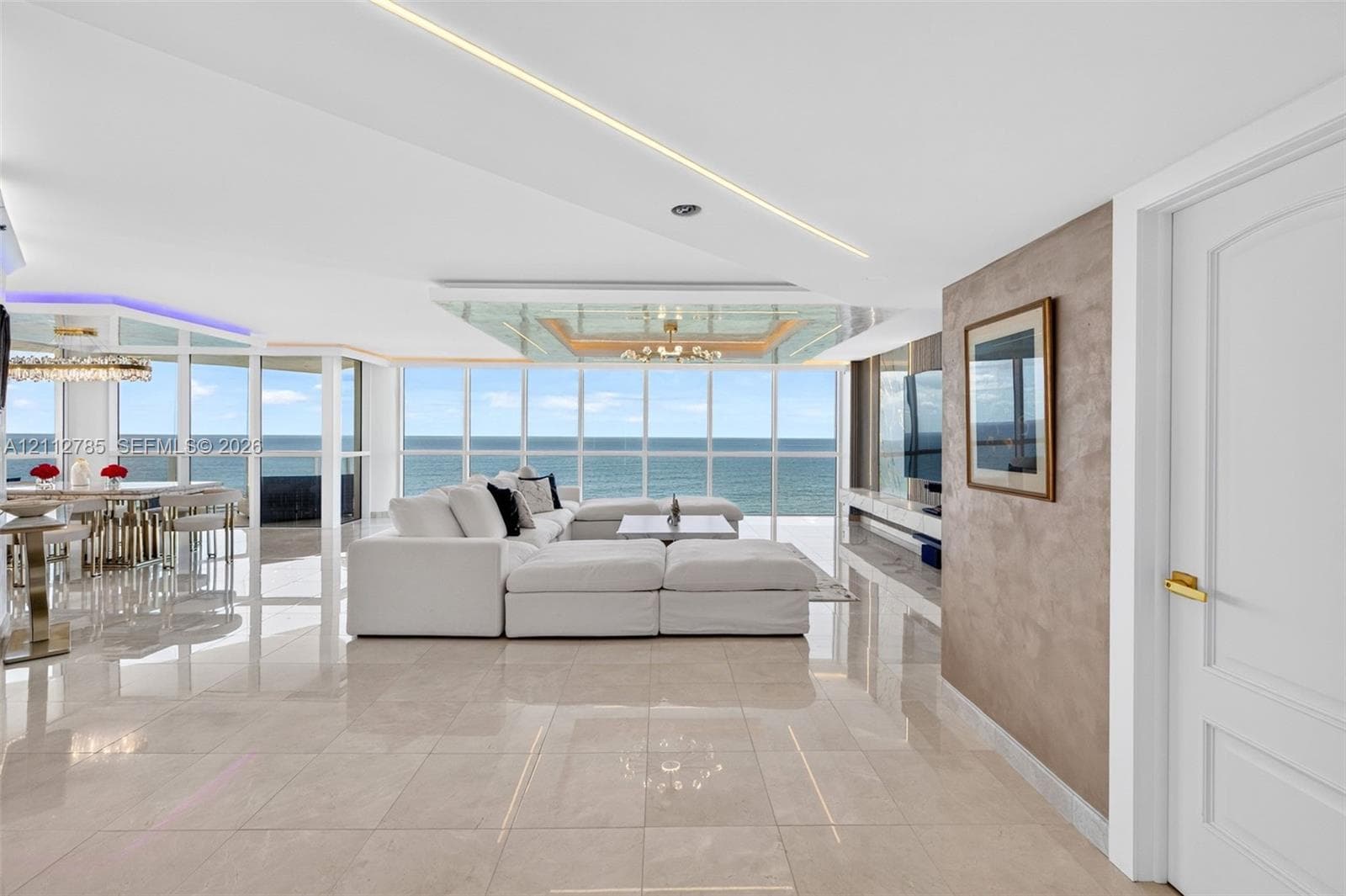 Floor-to-ceiling windows with ocean scenery, polished stone flooring, linear recessed ceiling lighting, and a custom textured accent wall
