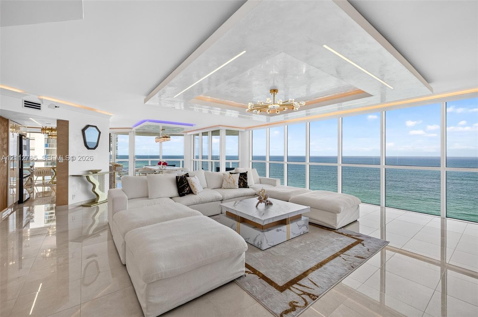 Floor-to-ceiling glass windows, recessed tray ceiling with accent lighting, polished tile flooring, and custom chandelier