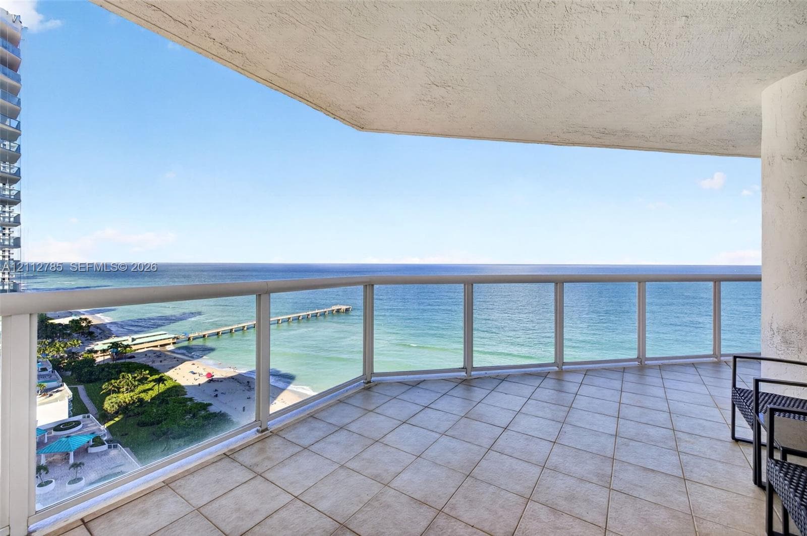 Covered balcony featuring square tile flooring and a glass railing system overlooking the oceanfront