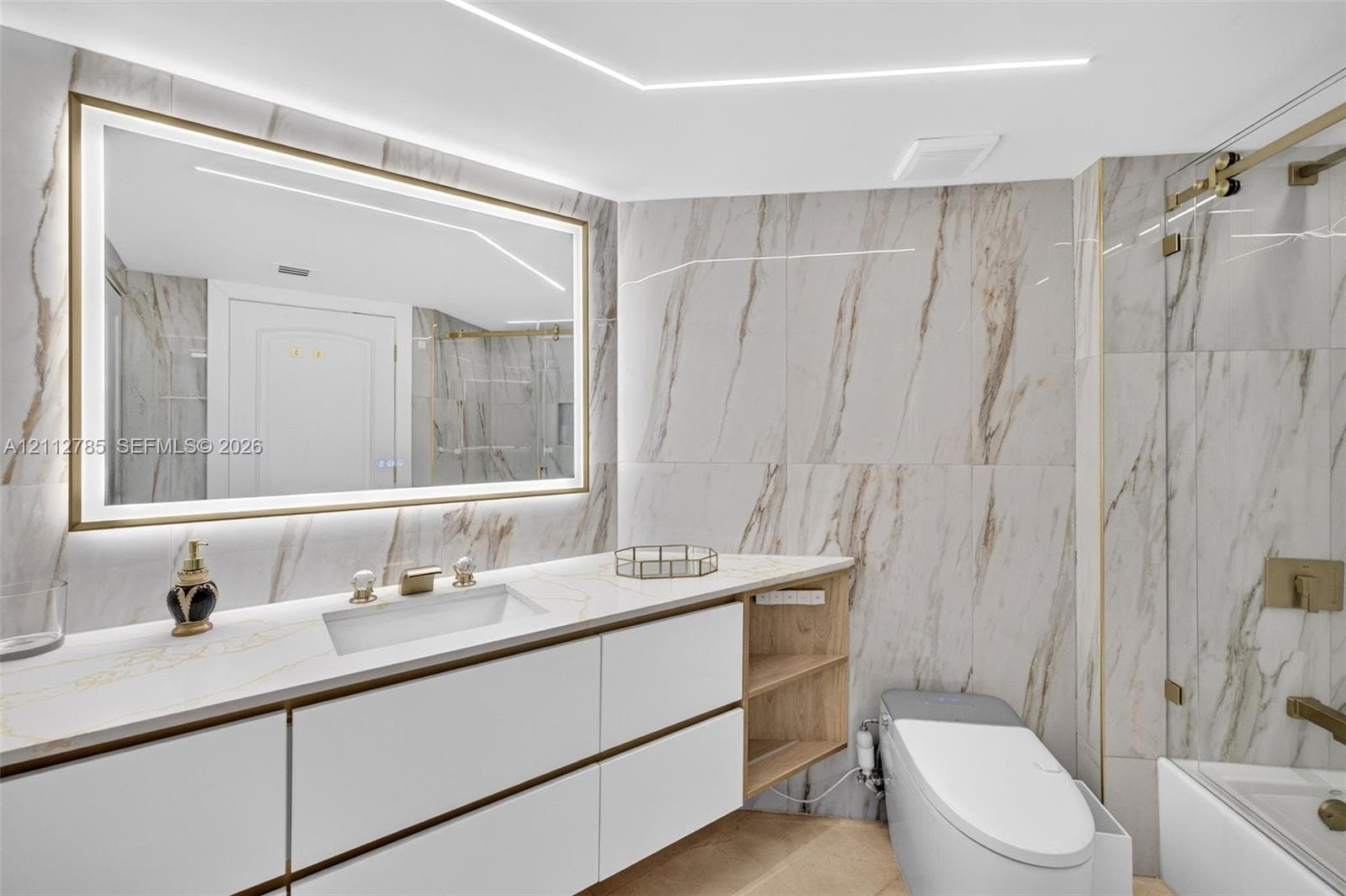 Bathroom featuring large-format stone-finish wall tile, a floating vanity with integrated cabinetry, an illuminated vanity mirror, and a glass-enclosed shower with metallic hardware