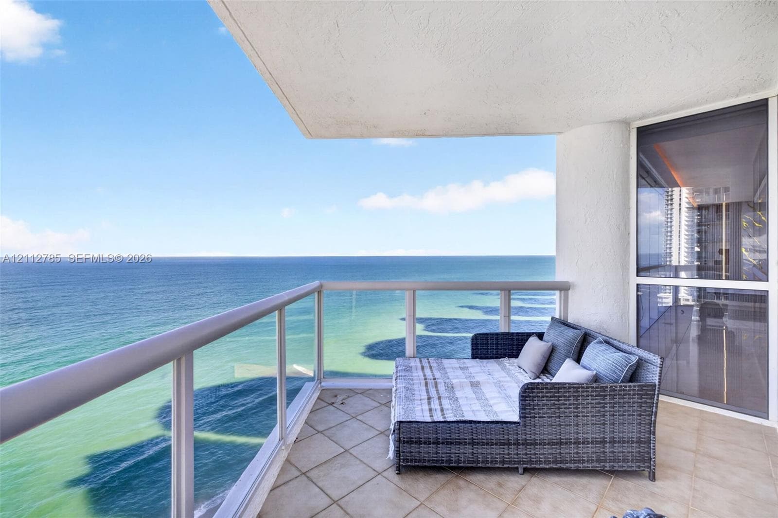 Covered balcony featuring tile flooring, glass and metal railings, and direct ocean water frontage