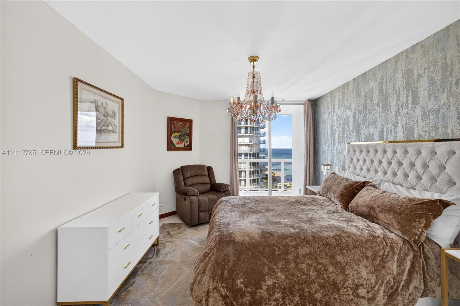 Textured accent wall, crystal chandelier, and floor-to-ceiling glass door opening to a private balcony