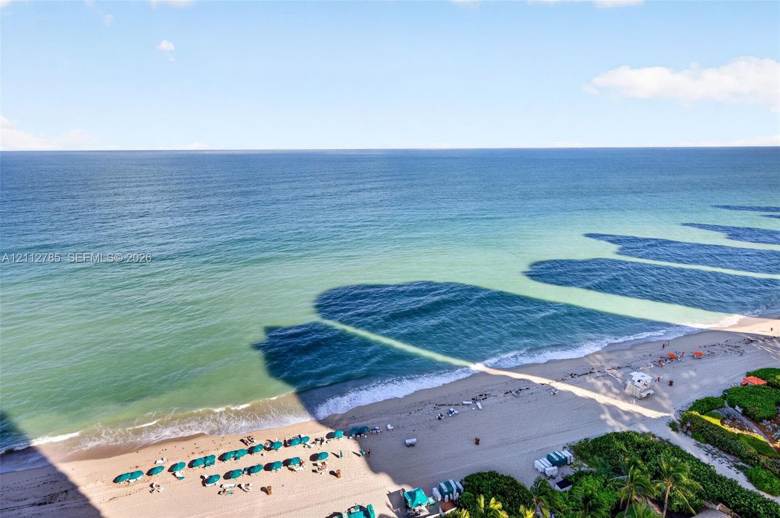 Oceanfront perspective featuring a wide stretch of sand, surf, and tropical vegetation