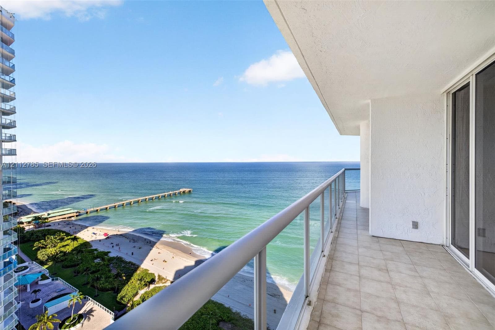 Covered balcony with light-colored floor tiling, glass panel railing, and oceanfront exposure