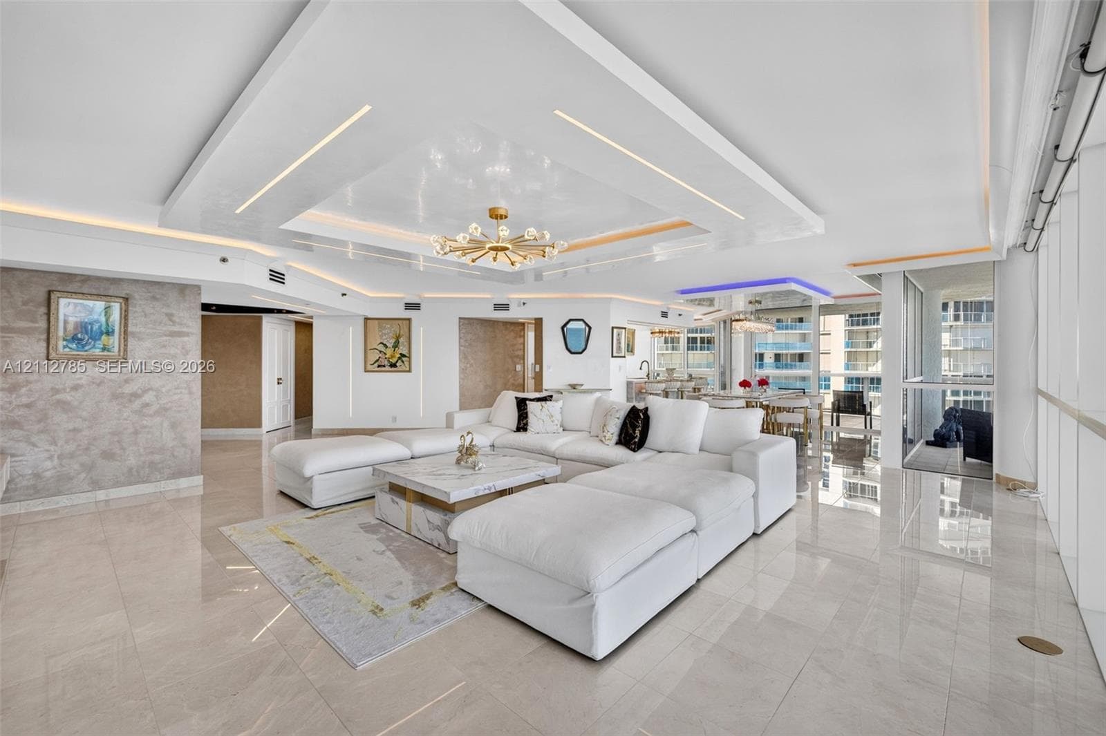 Open-concept living area featuring a custom recessed tray ceiling with integrated lighting, polished stone-finish flooring, floor-to-ceiling windows, and a textural wall finish