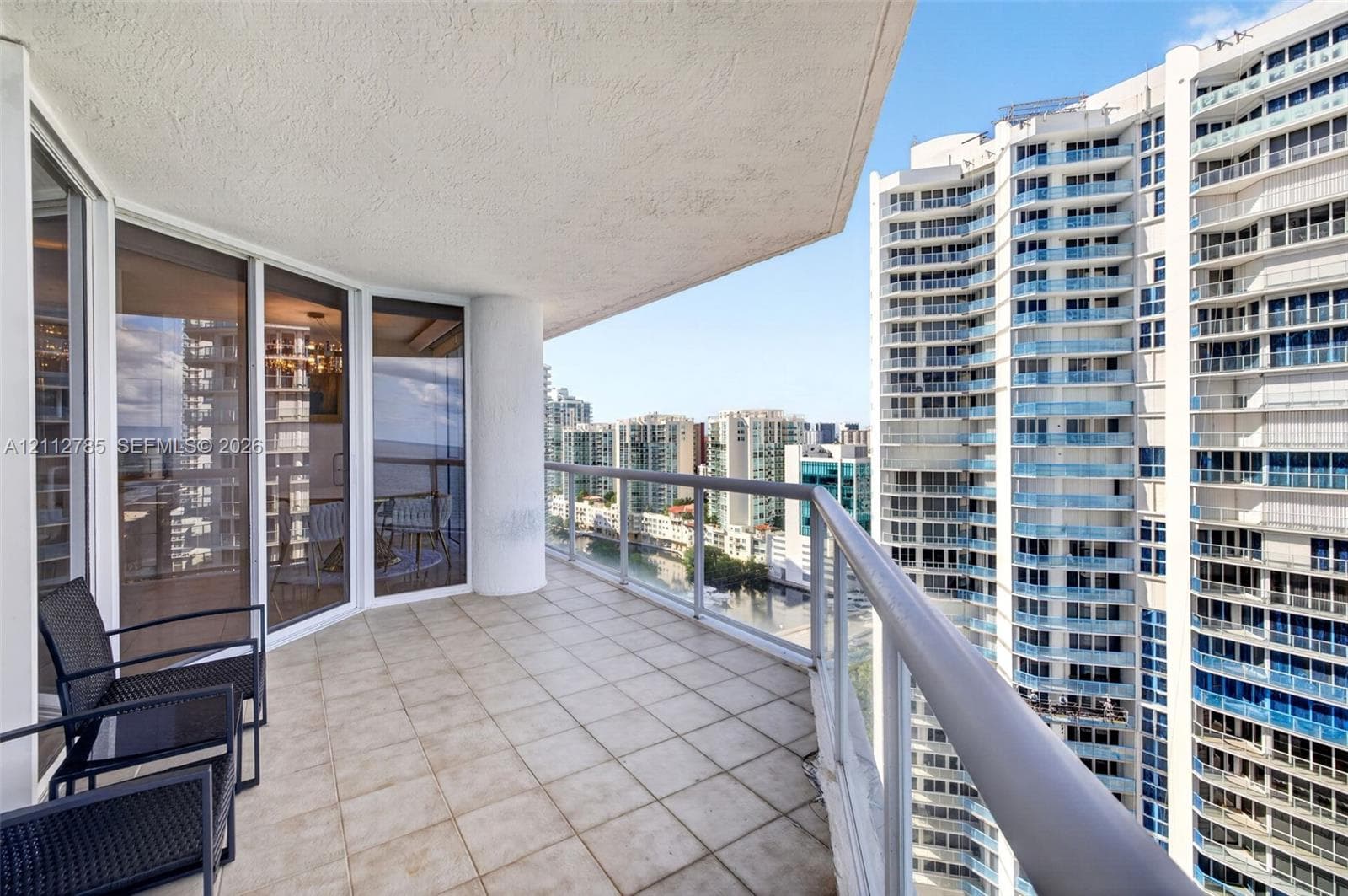 Covered wrap-around balcony featuring ceramic tile flooring, a metal-framed glass railing, and floor-to-ceiling glass sliding doors
