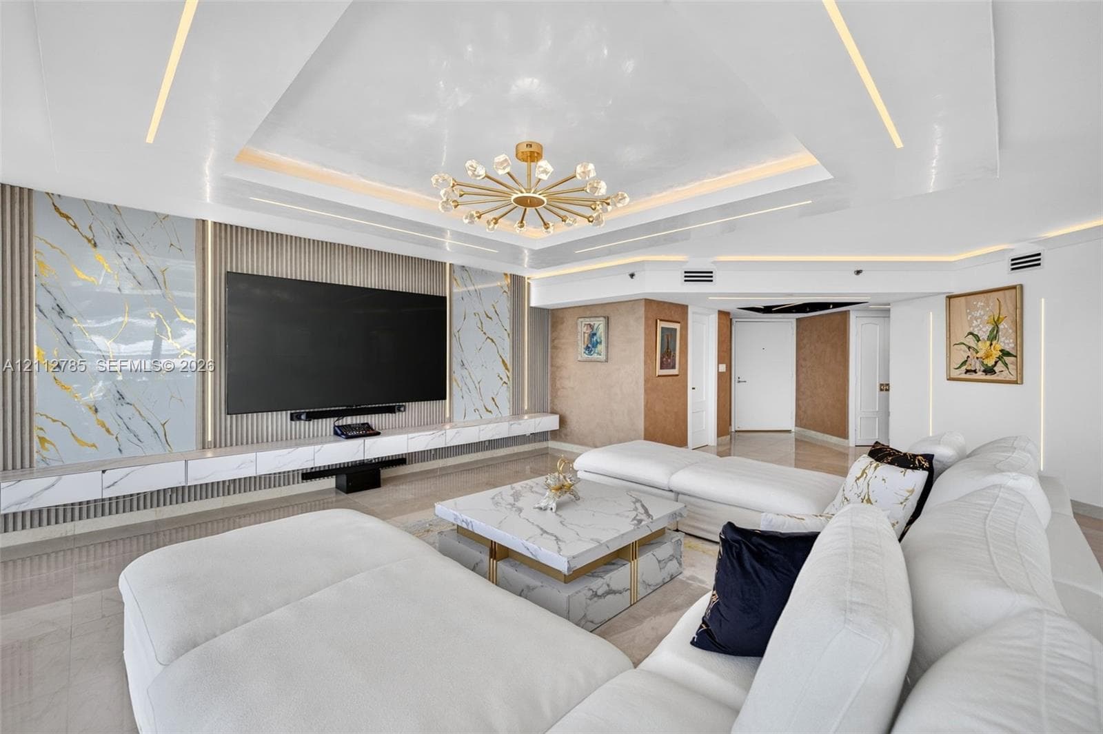 Tray ceiling featuring integrated perimeter lighting, custom stone-panel wall accents, recessed linear lighting, and a modern multi-arm chandelier