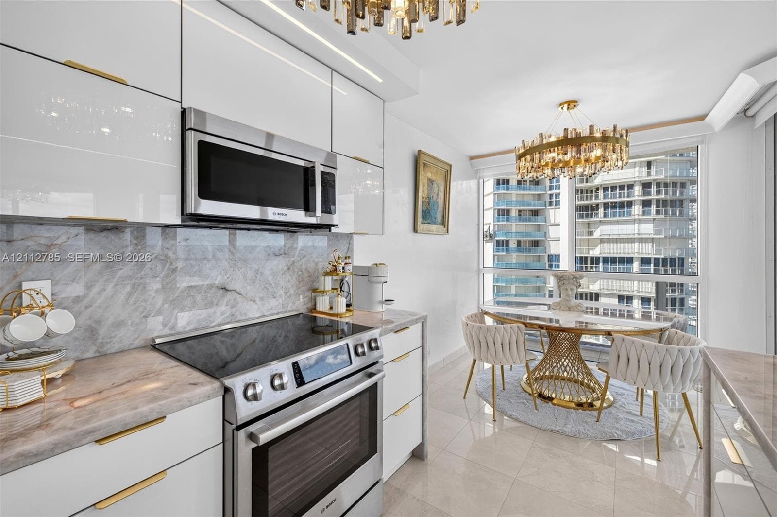 Kitchen featuring high-gloss white cabinetry, gold-tone hardware, stone-surface countertops, stone-tile backsplash, and integrated stainless steel appliances