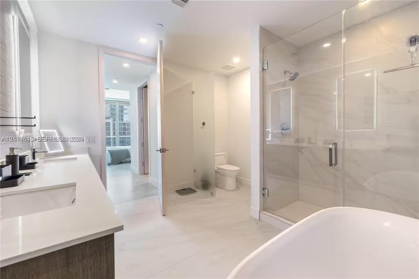 Bathroom featuring a dual-sink vanity with light-colored countertops, a freestanding soaking tub, and a glass-enclosed shower with tiled surround