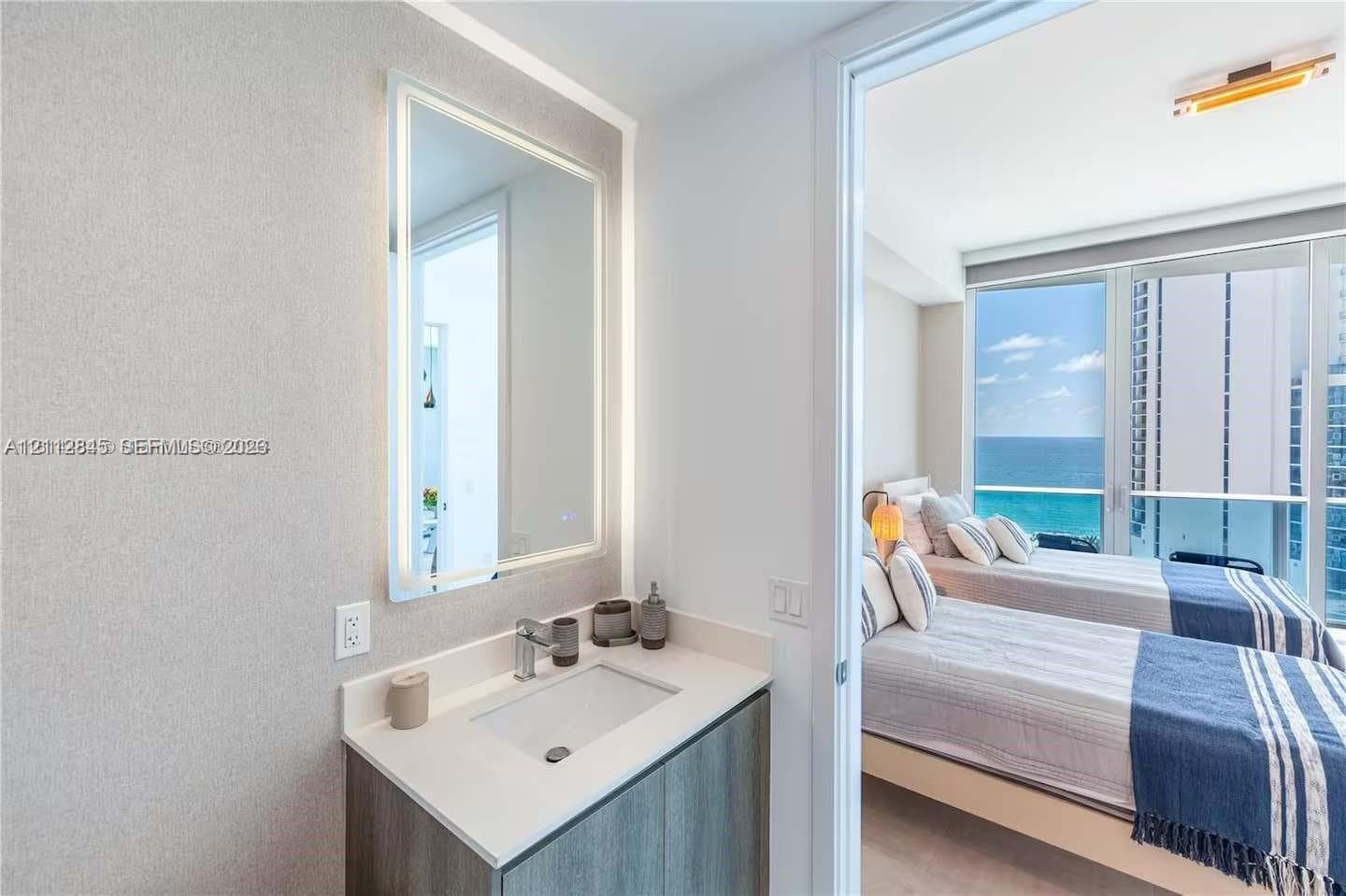 Vanity featuring a stone-composite countertop, undermount sink, integrated LED-backlit mirror, and wood-finish cabinetry, paired with floor-to-ceiling glass windows and an exterior balcony