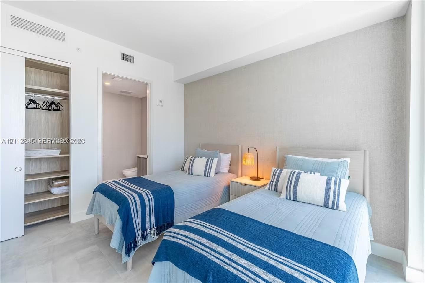 Bedroom featuring neutral-toned textured wall covering, wood-finish shelving within an integrated closet, and light-toned flooring